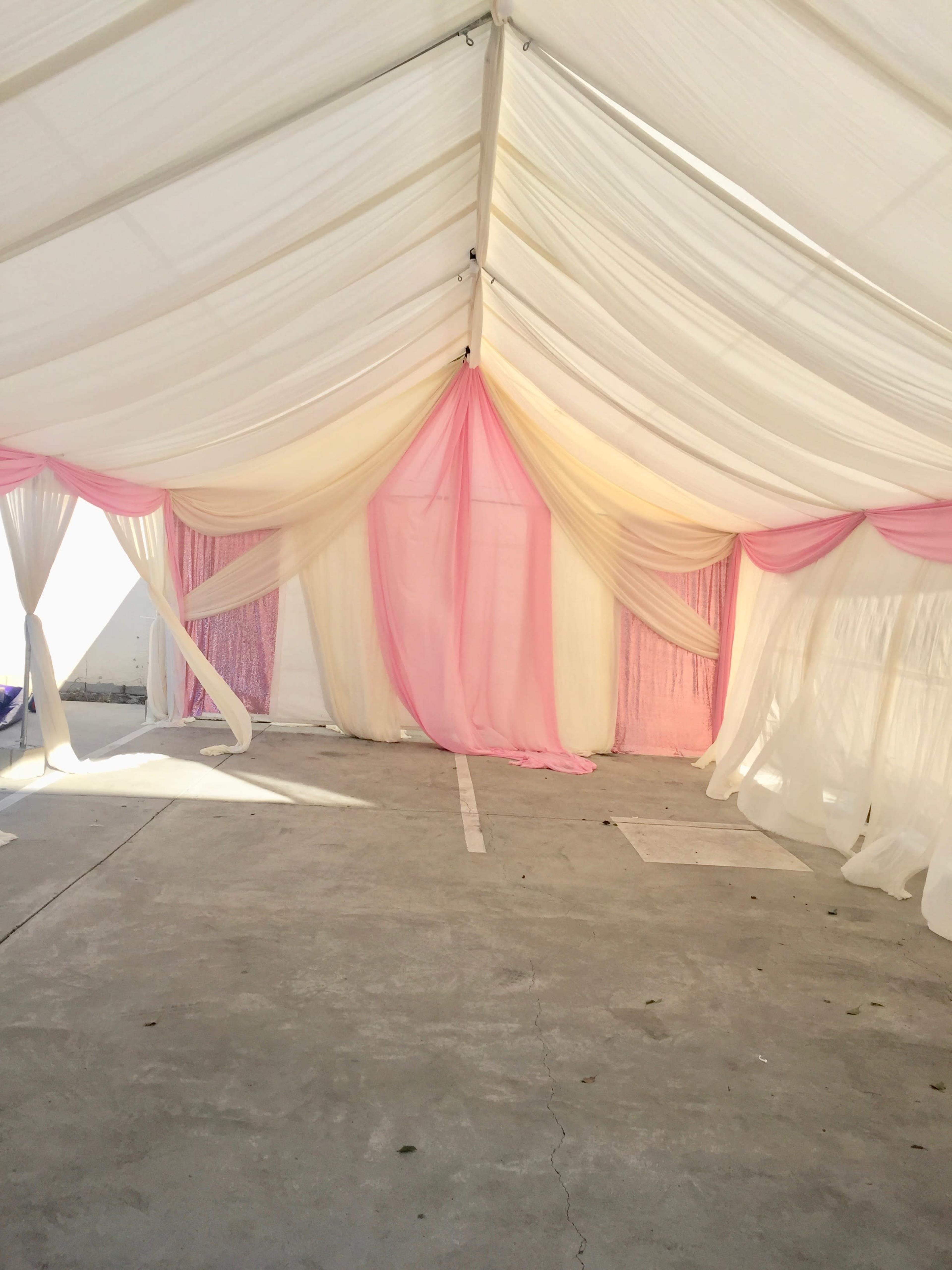 The interior of a tent is adorned with draped fabric in white and soft pink, creating a decorative entrance and an airy atmosphere.