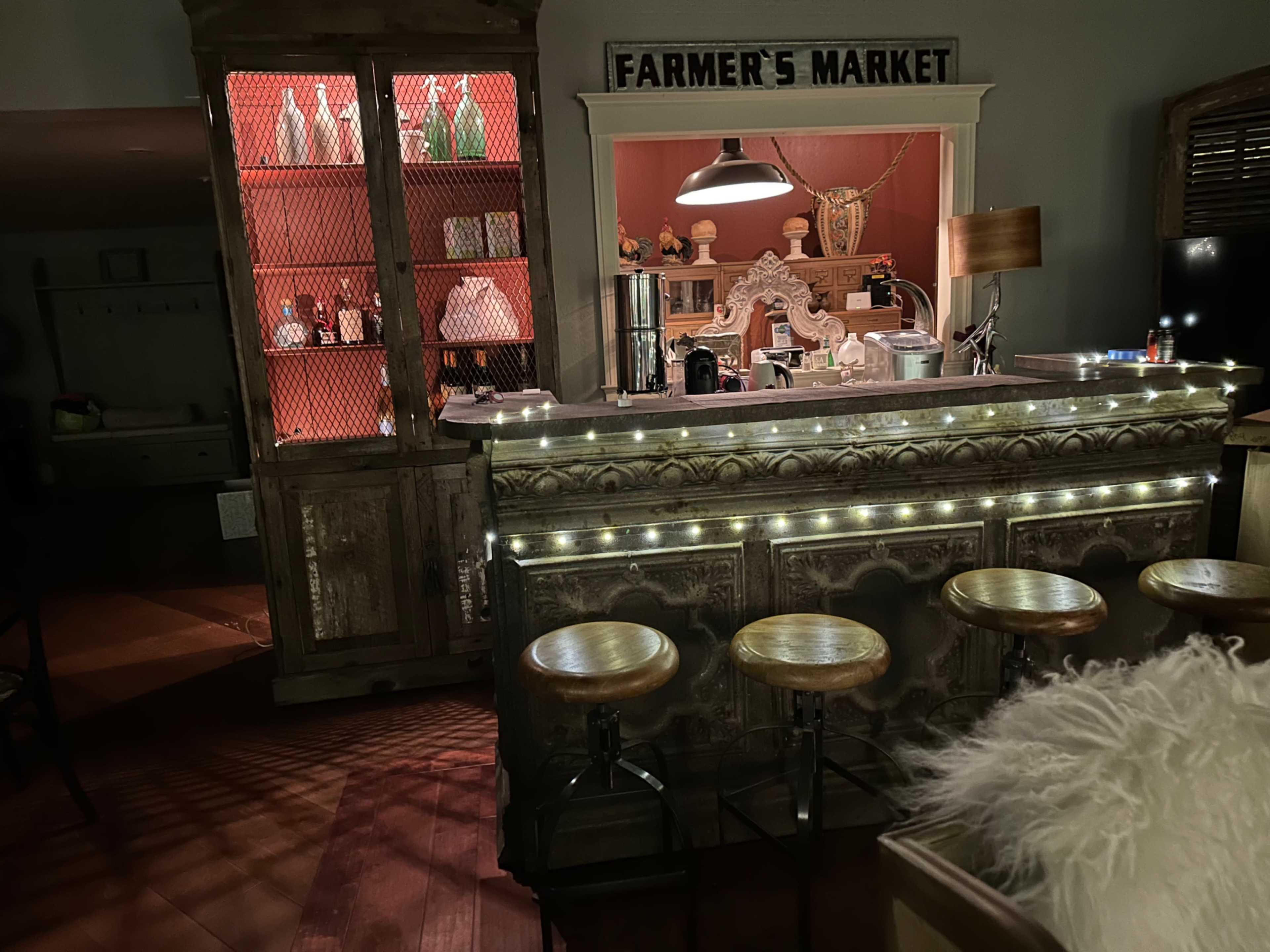 A rustic bar area with wooden stools, a decorative counter, and a vintage display cabinet labeled "FARMER'S MARKET."