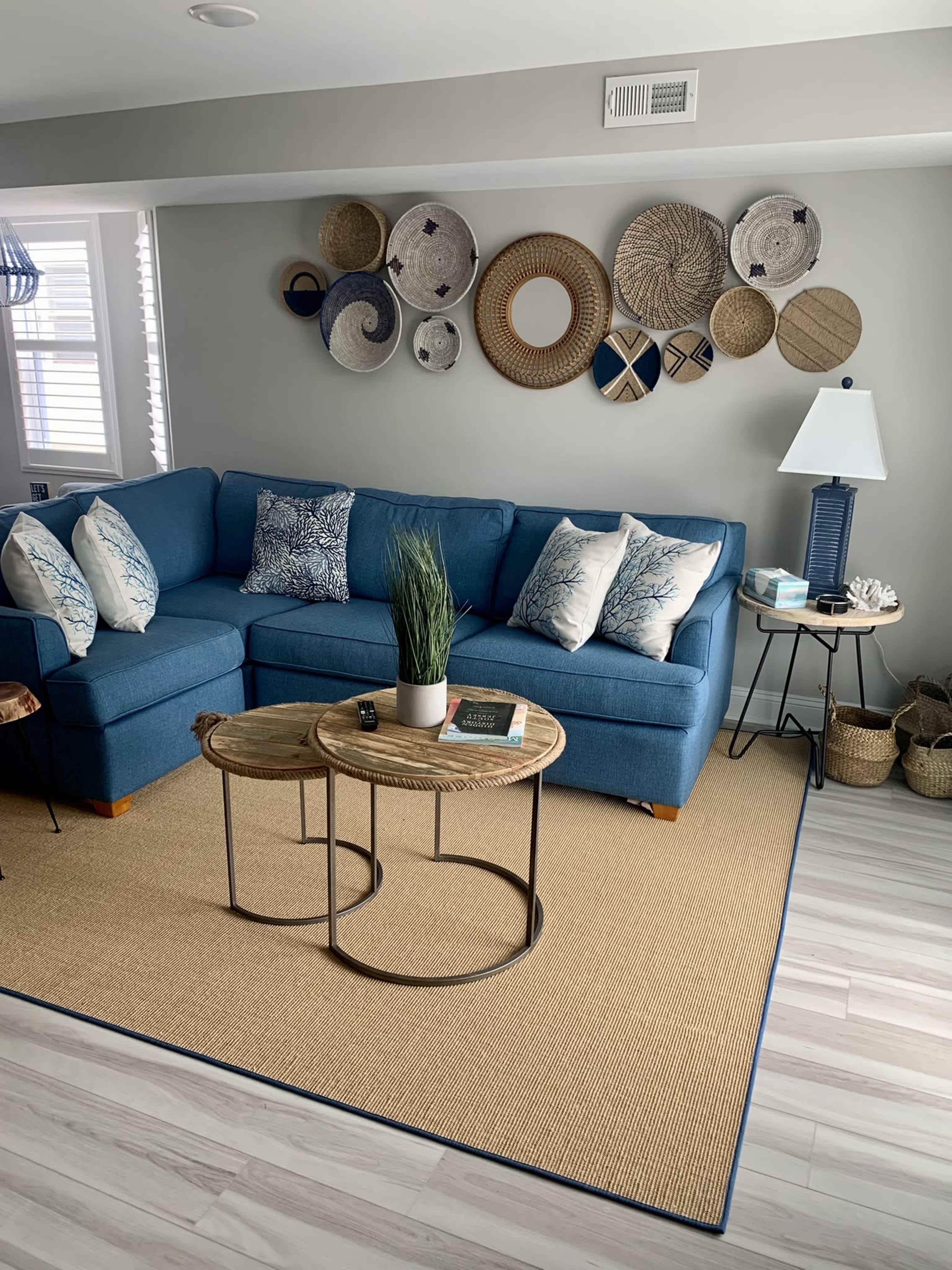 A living room corner with a blue sectional sofa adorned with patterned pillows, two coffee tables, and decorative wall baskets.