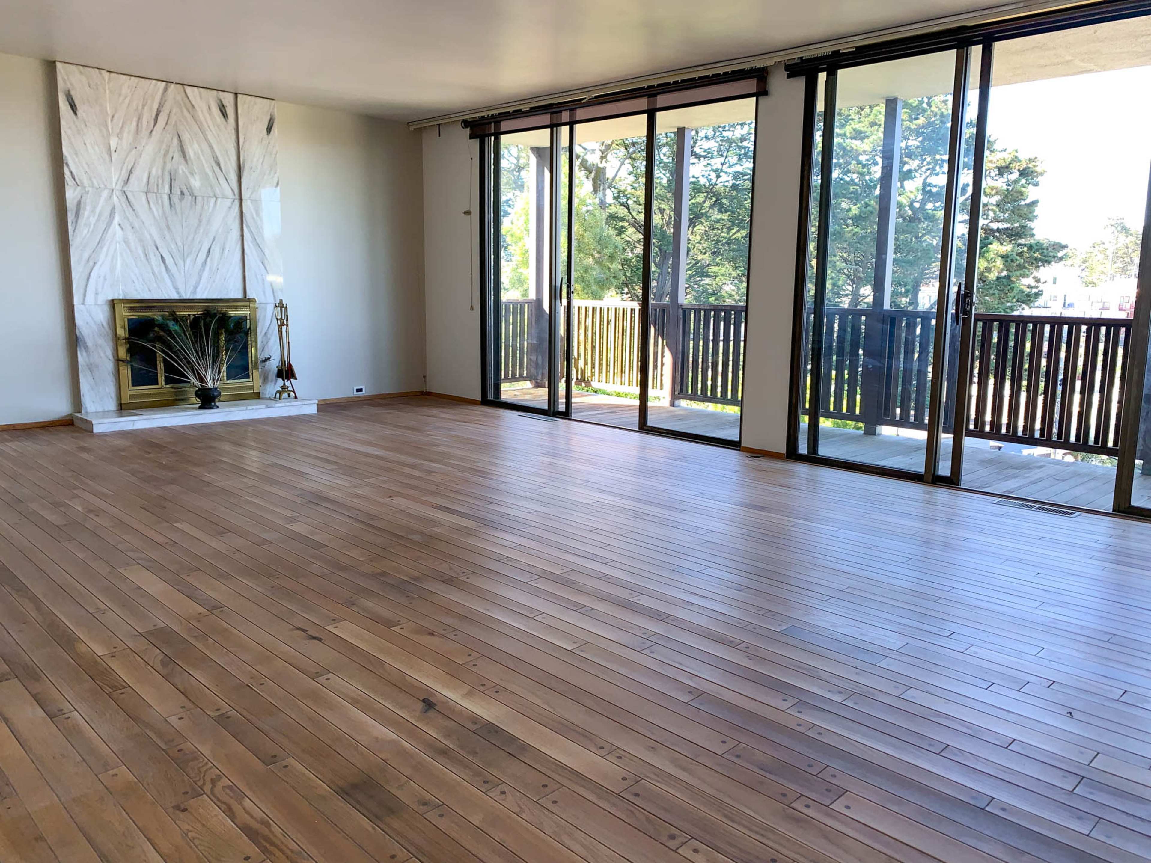 A spacious room with wooden floors, large windows, and a fireplace against a white marble wall.