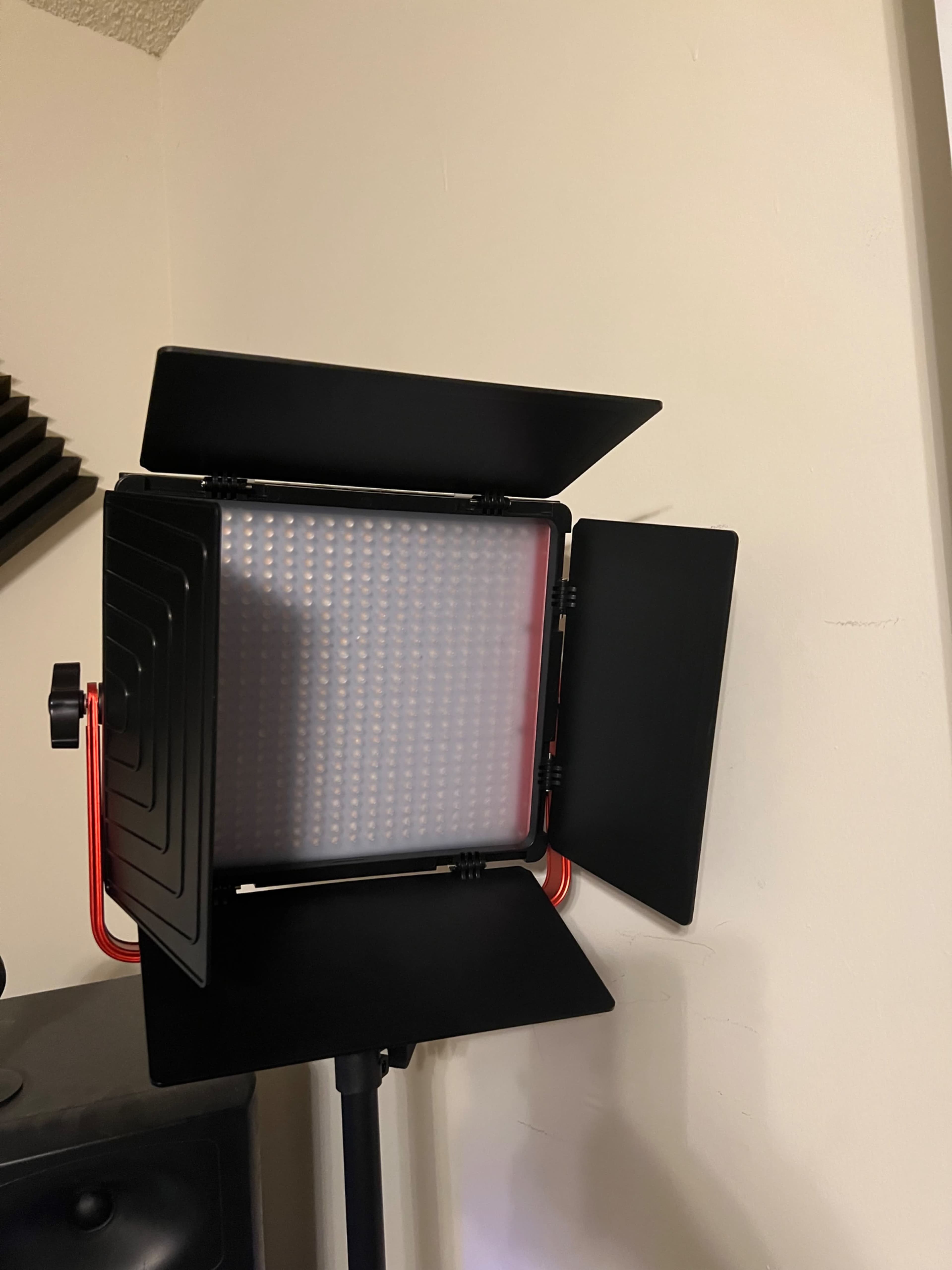 A studio LED light with barn doors is positioned against a plain wall.