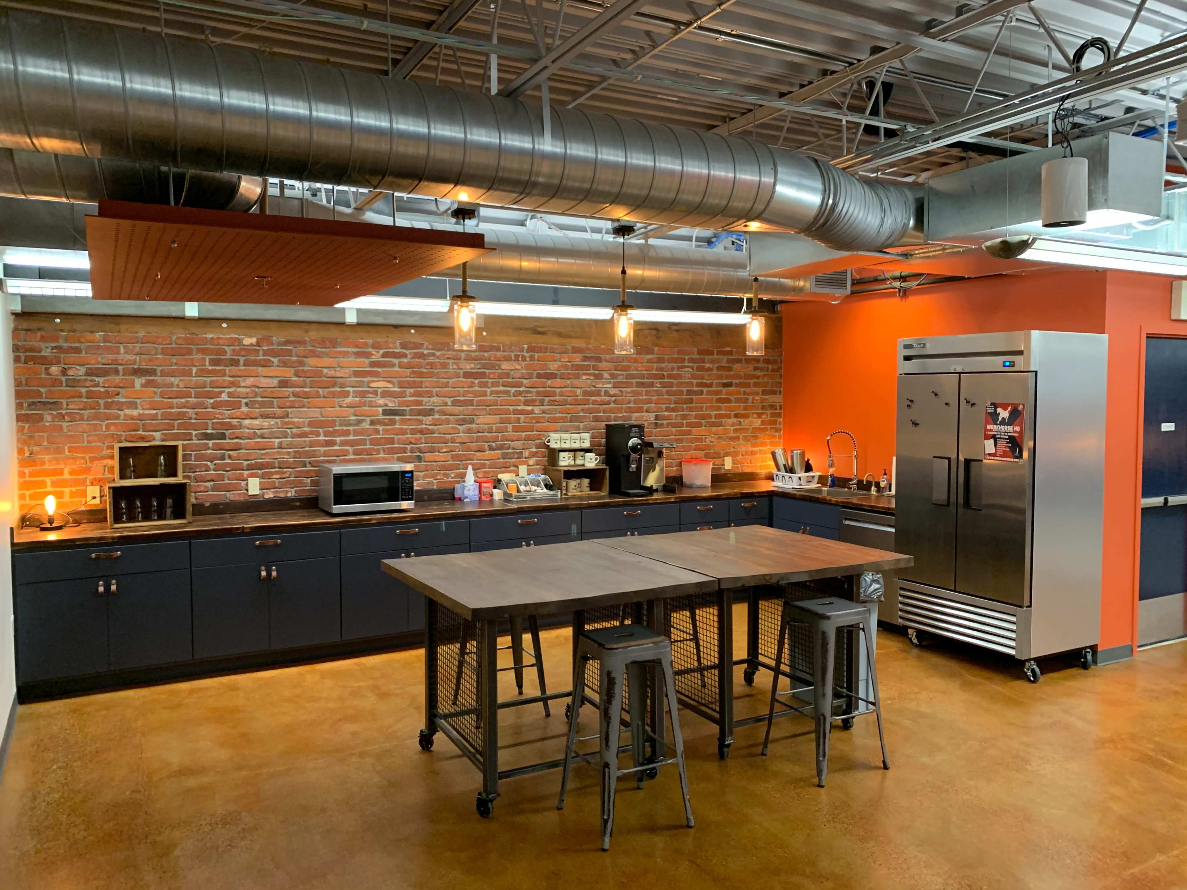 A modern kitchen featuring brick walls, a central metal table, and stainless steel appliances.