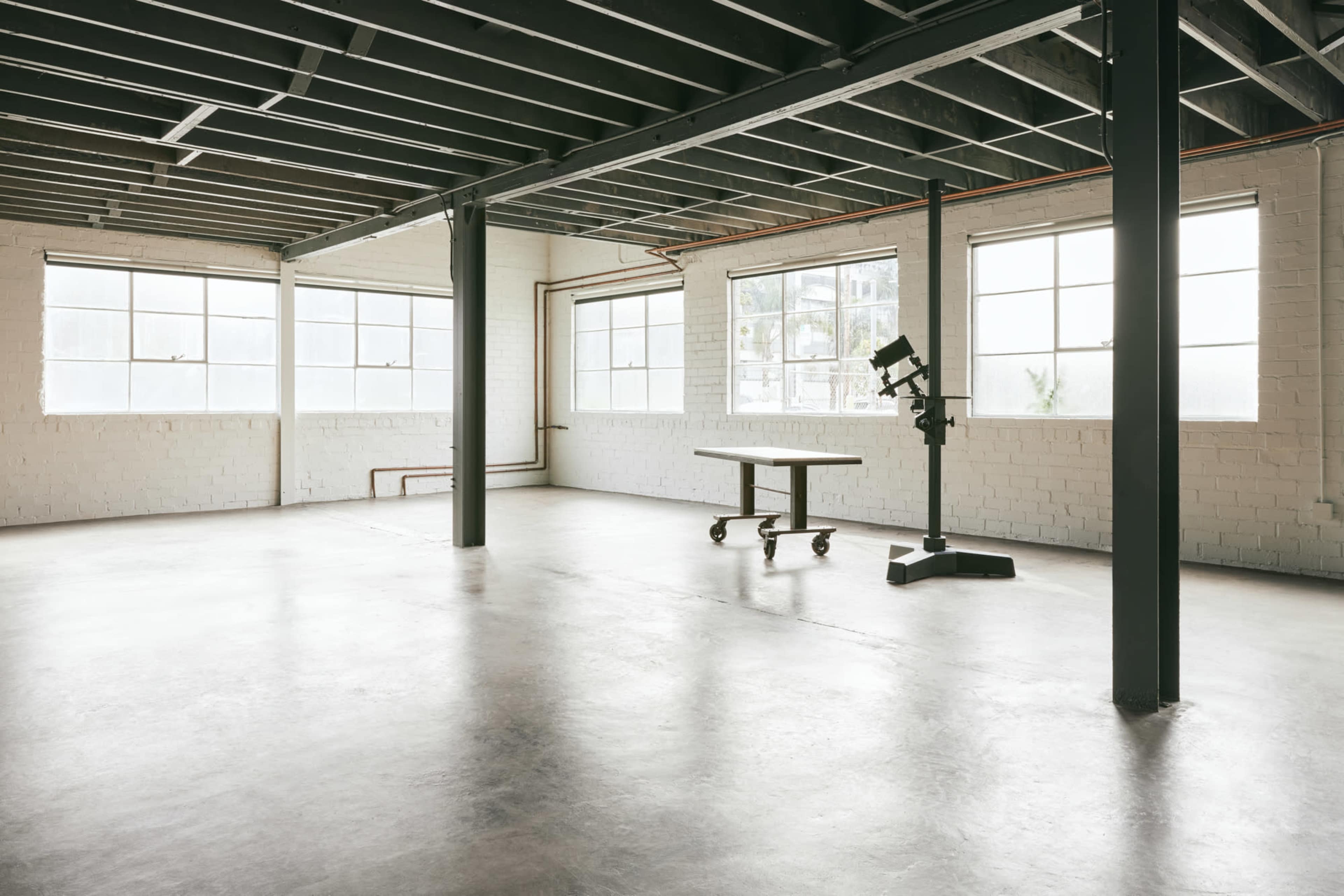 A spacious, empty interior room with large windows, a minimalistic table, and a standing lamp.