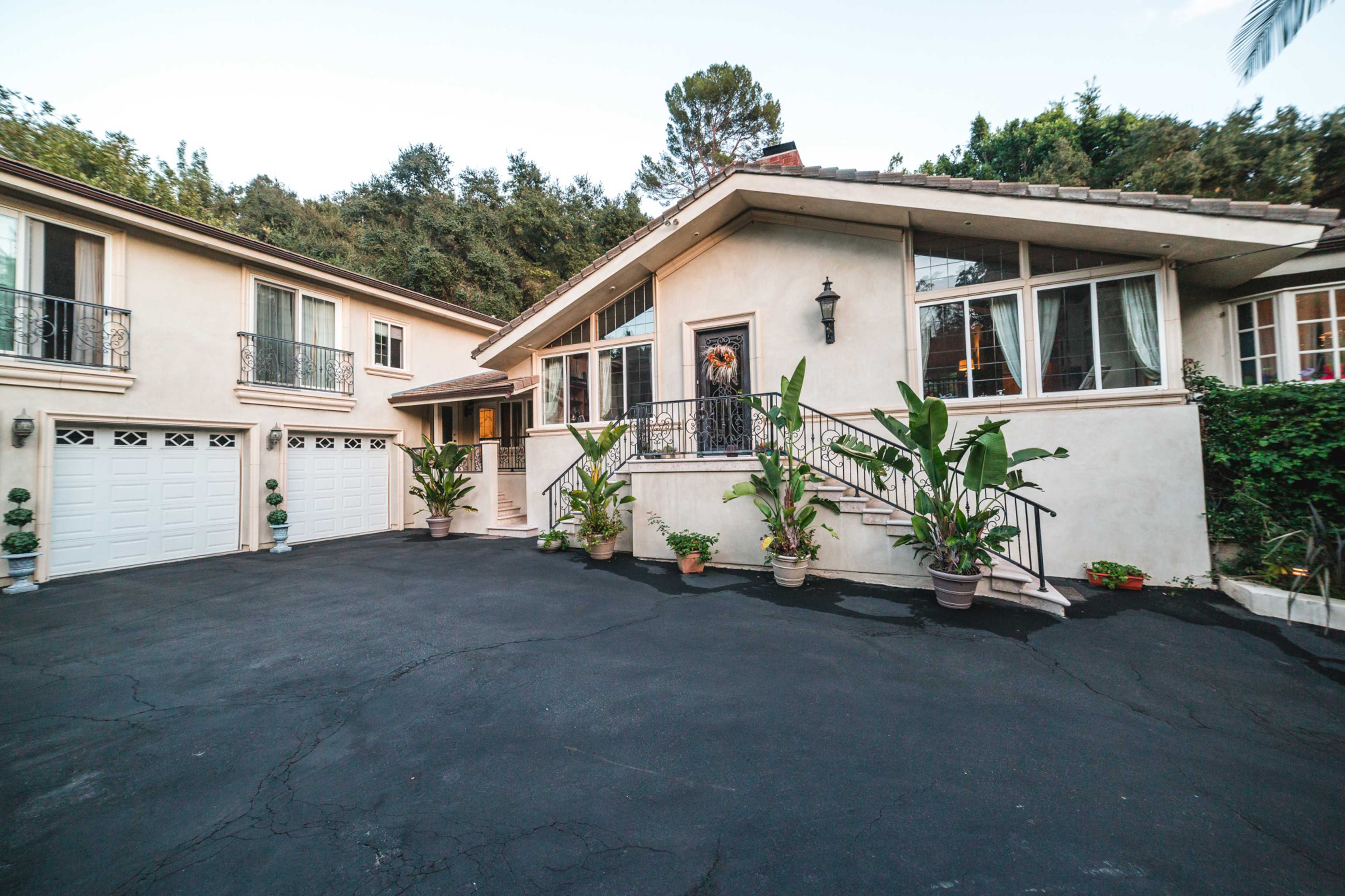 A house with a large driveway and several potted plants, featuring a prominent front entrance and garage doors on either side.