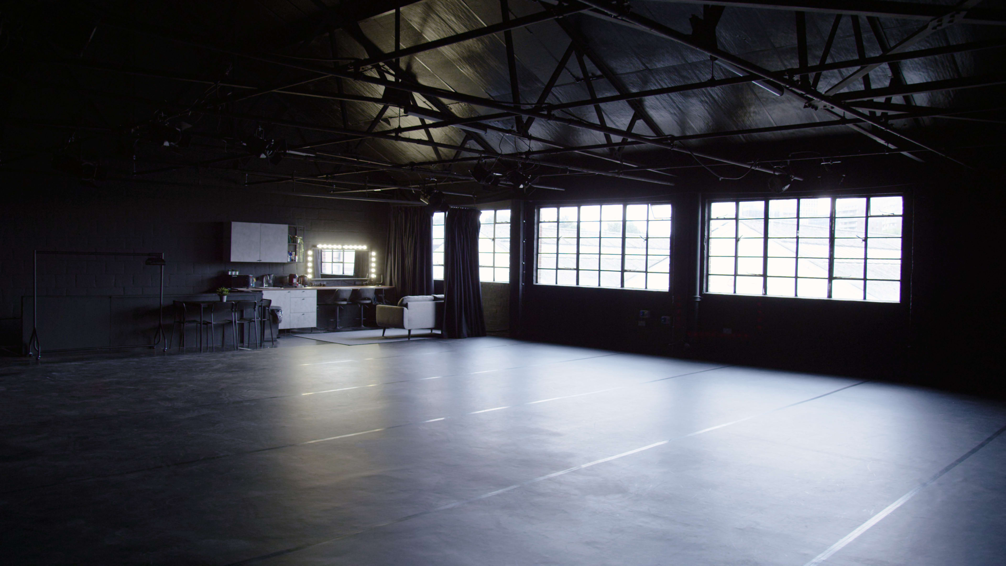 A spacious, dimly lit studio with large windows and a row of mirrors against one wall.