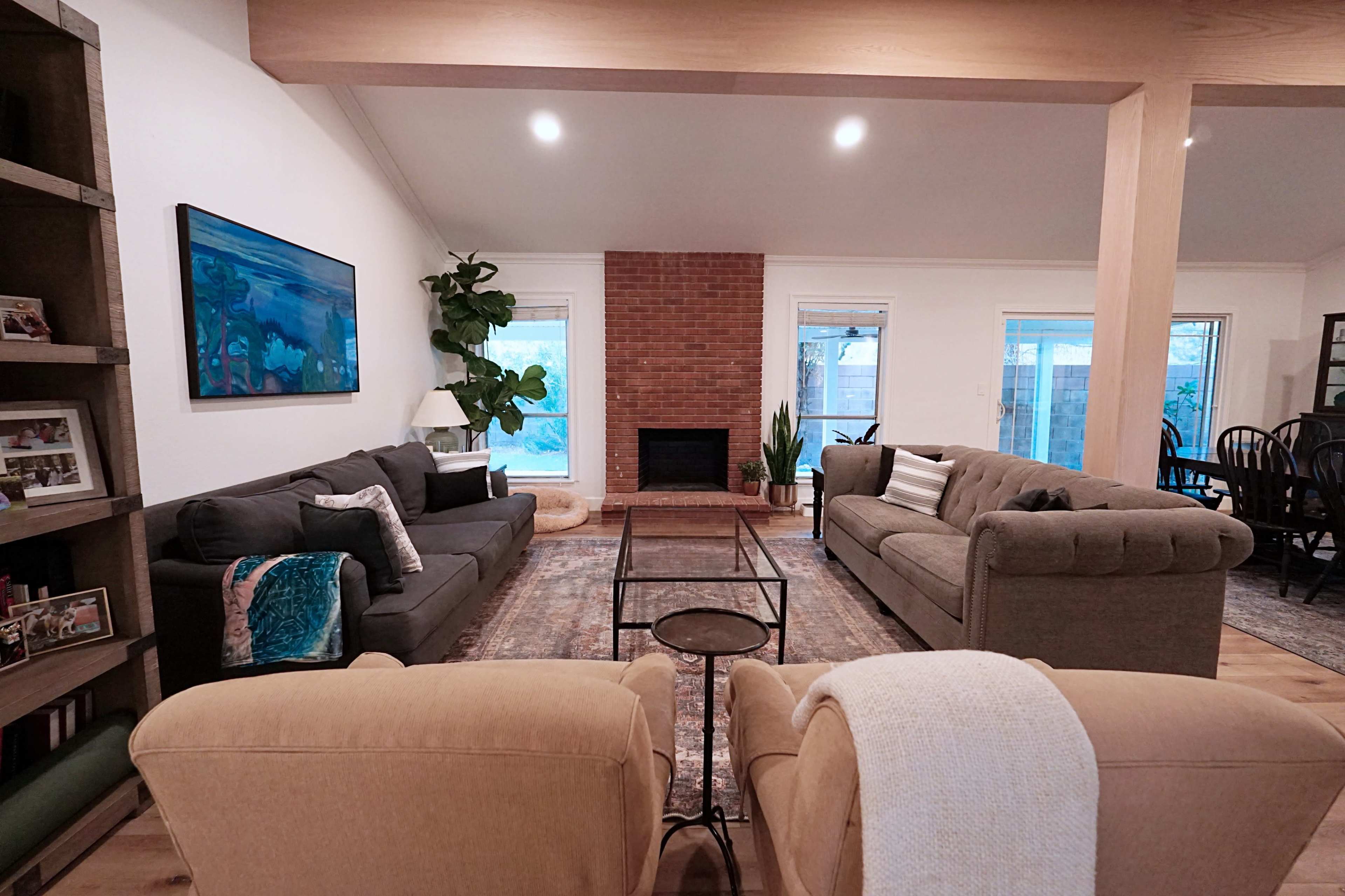 The living room features two gray sofas facing each other, a coffee table in the center, and a brick fireplace flanked by windows.
