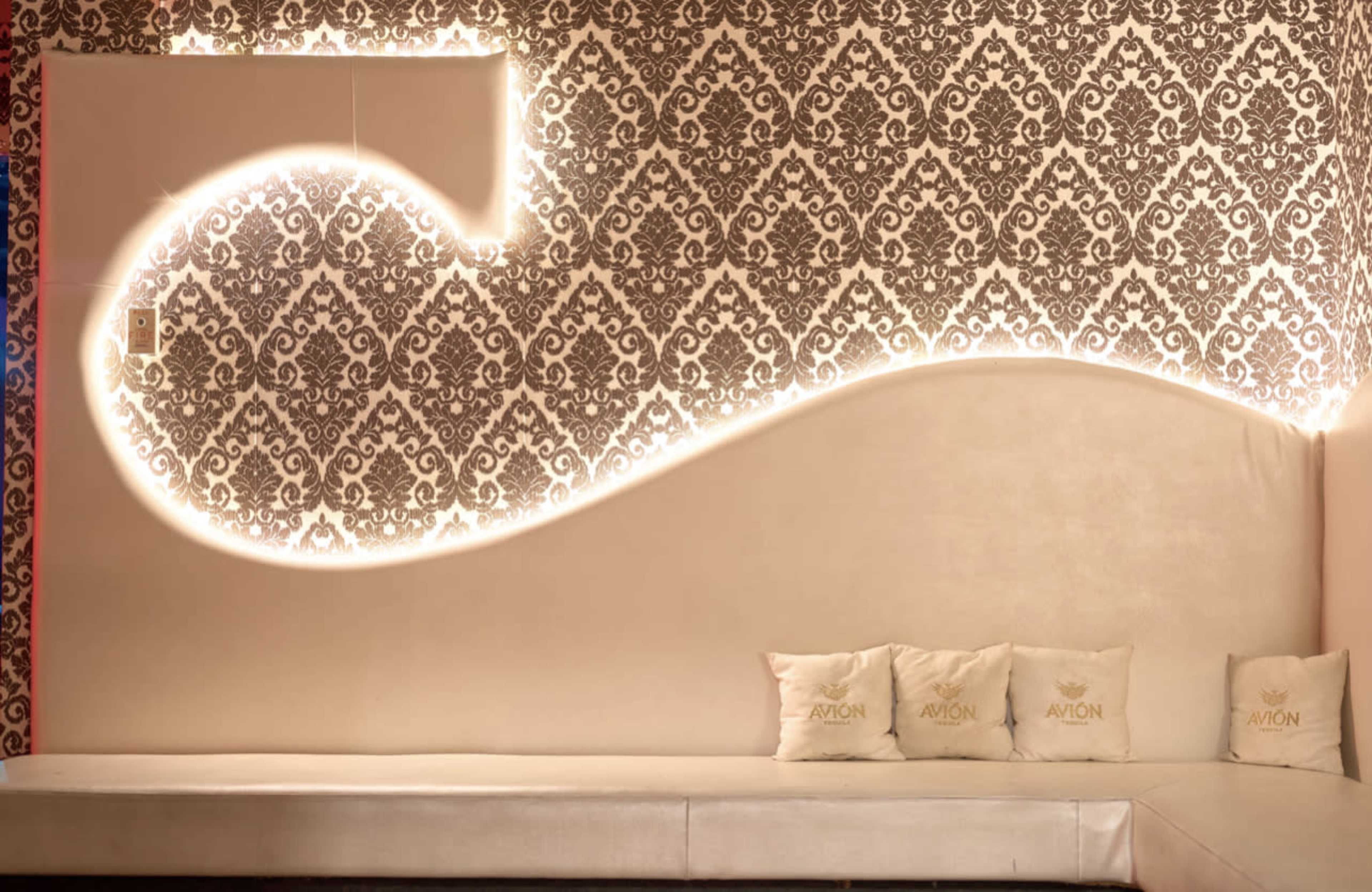 A modern seating area with a curved, illuminated design on the wall and decorative pillows arranged on a sleek bench.