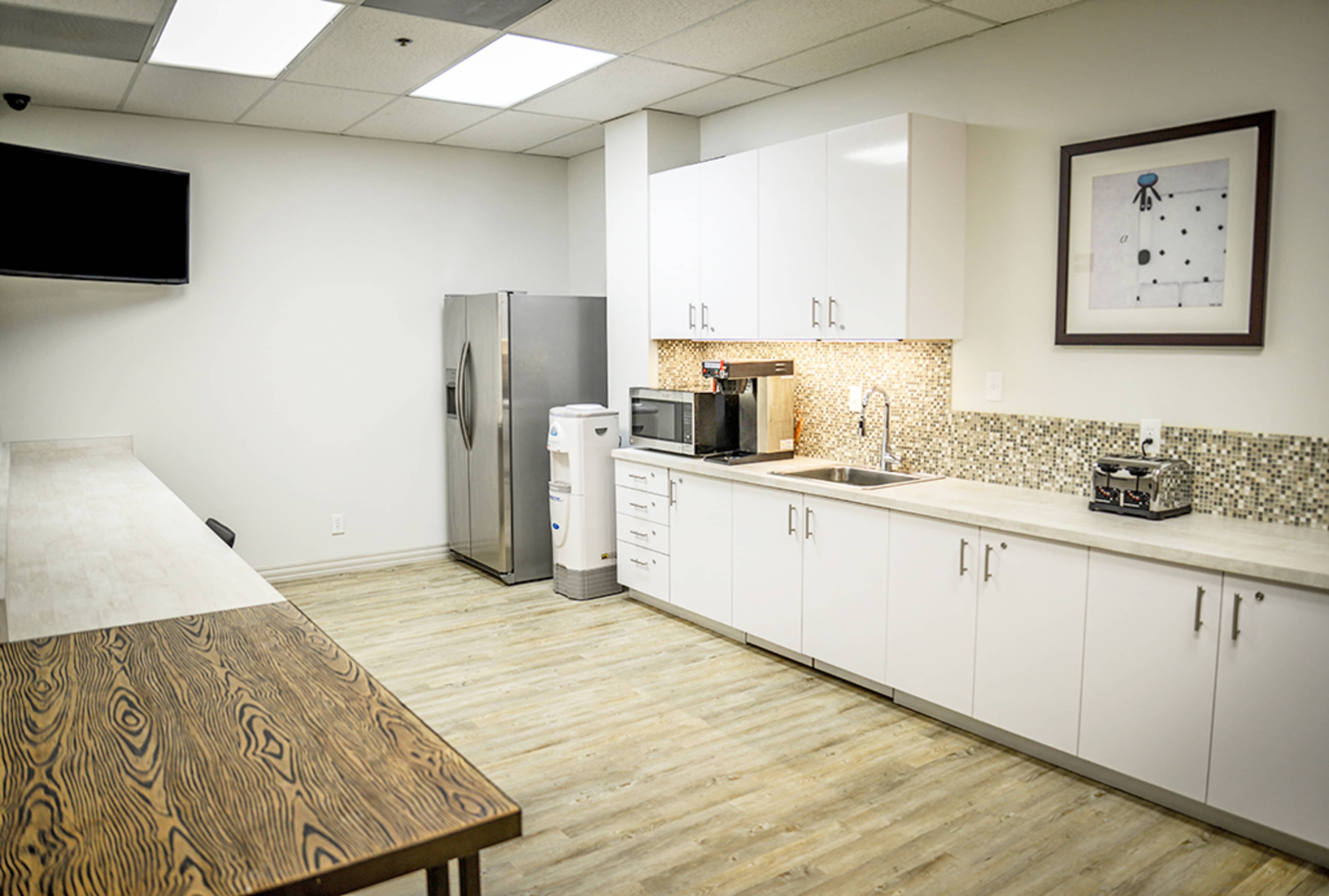 A modern break room featuring a refrigerator, microwave, sink, and a wooden table with chairs.