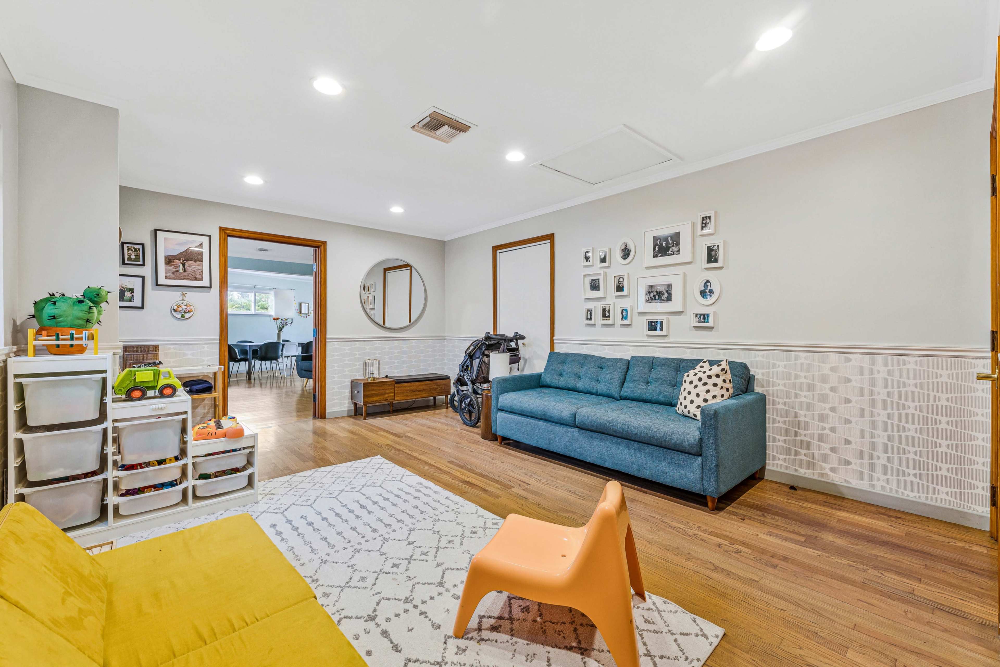 The image shows a living room featuring a blue sofa, a yellow chair, and a play area with storage bins.