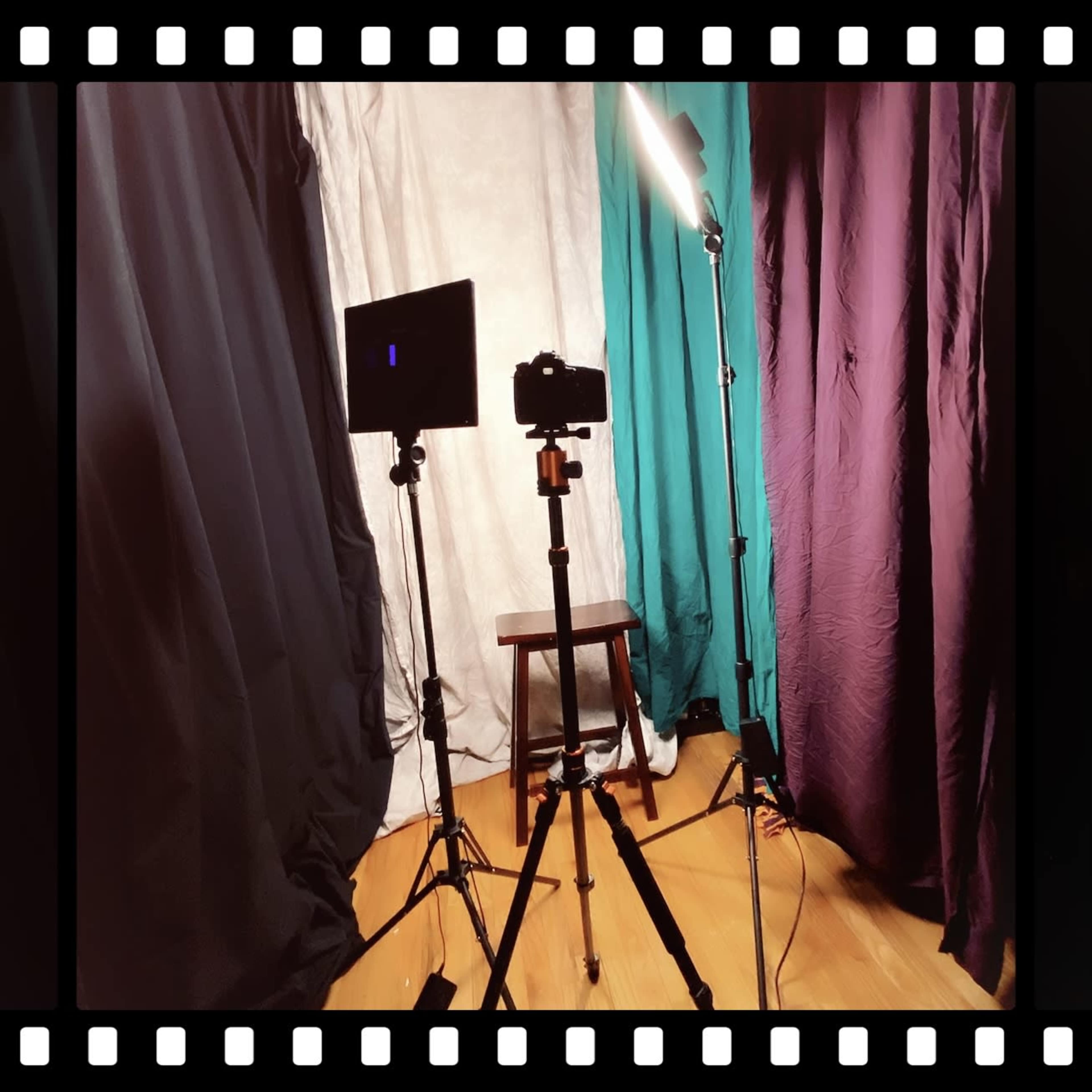 A photography setup with a camera on a tripod, a light stand, and a stool surrounded by various draped fabrics.