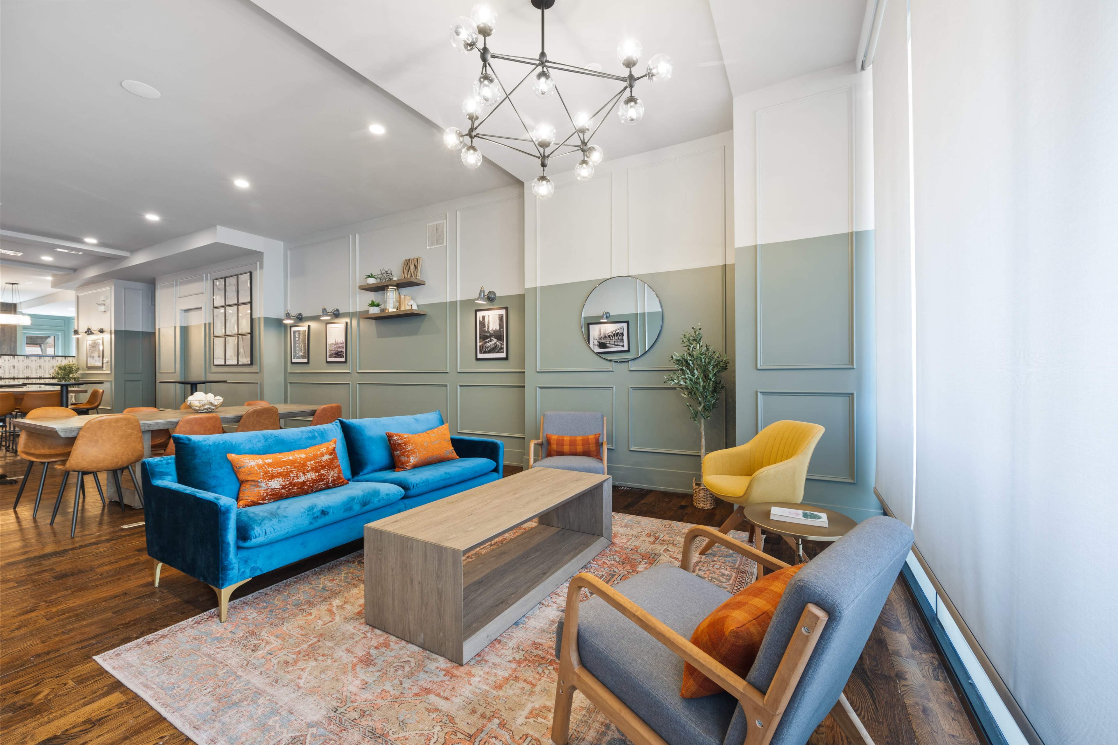 A modern living space features a blue sofa, light wooden coffee table, and yellow armchair, complemented by a decorative chandelier and a mix of wall colors.