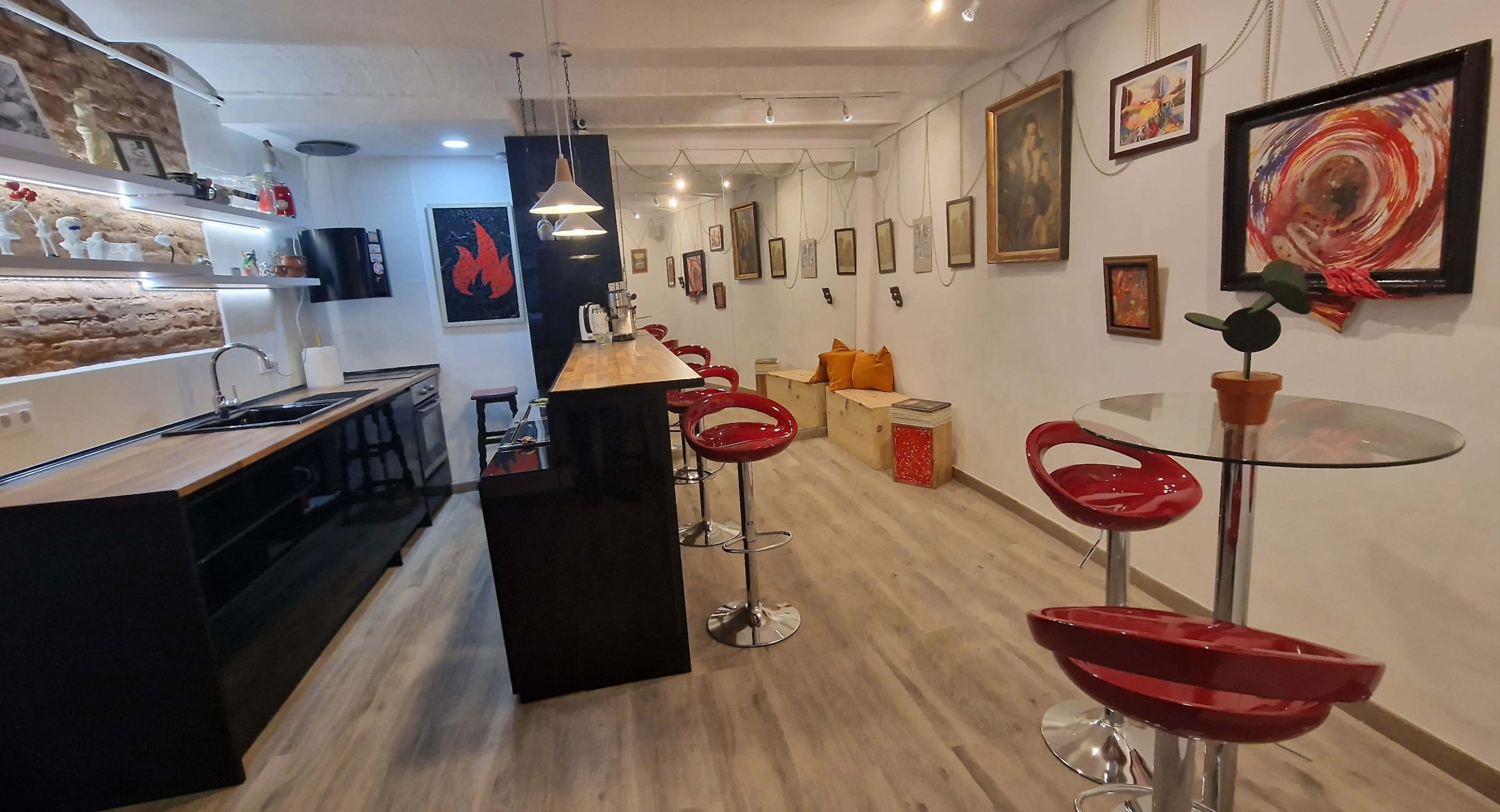 A modern kitchen and dining area with a bar counter, red stools, and artwork on the walls.