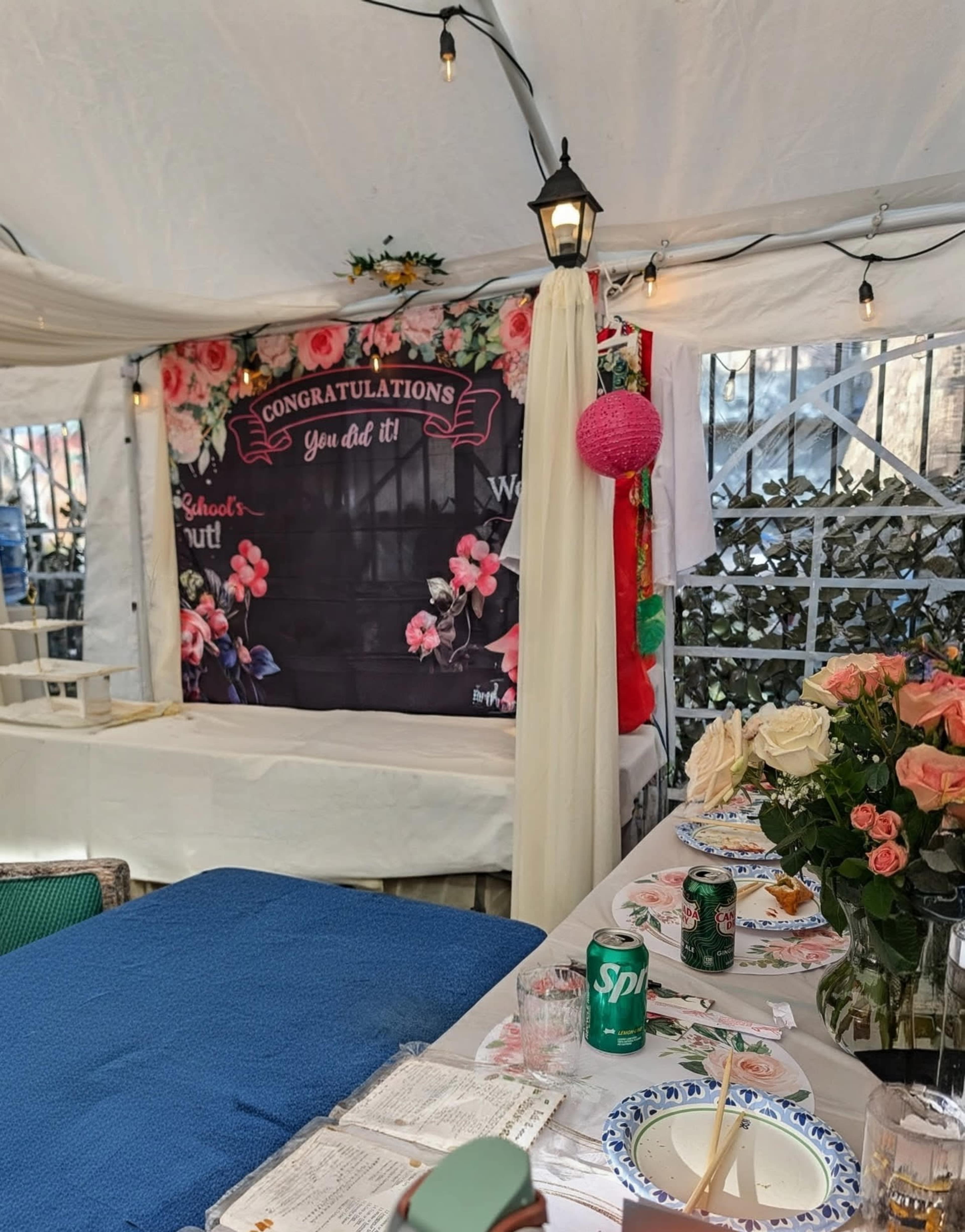 A decorated tent features a "Congratulations" banner, floral arrangements, and a festive table set for a celebration.