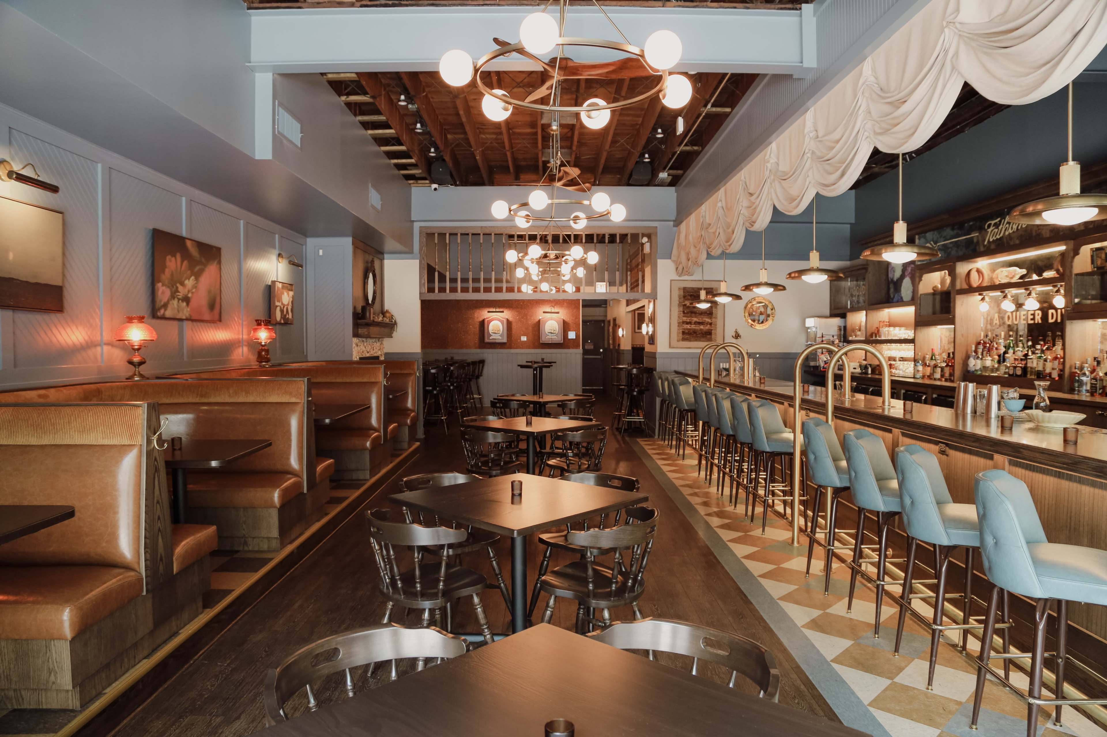 The image shows a stylish, modern restaurant interior with a bar, several booth seating areas, and decorative lighting fixtures.