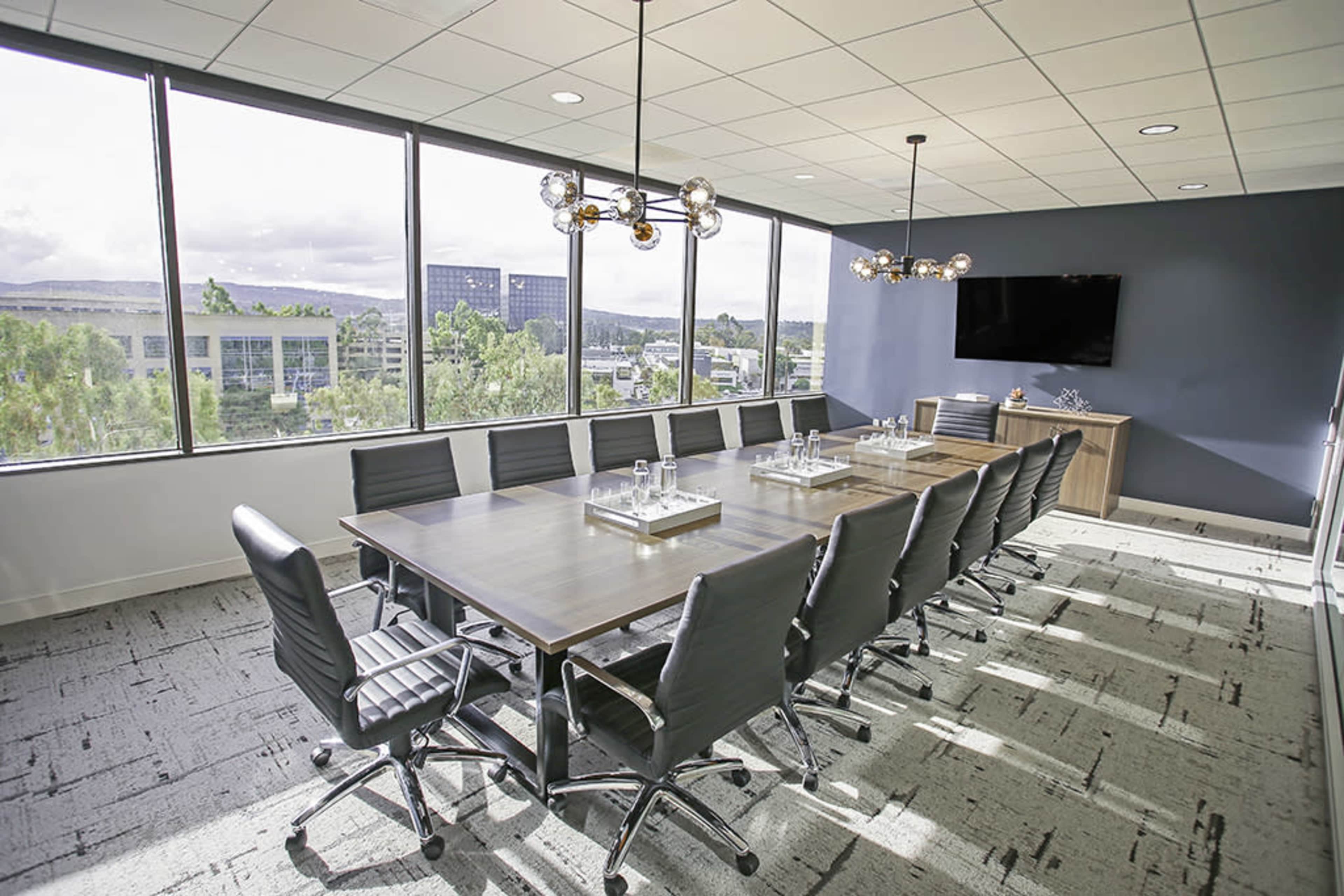 A modern conference room features a large table surrounded by black leather chairs, with large windows providing a view of the outdoors.