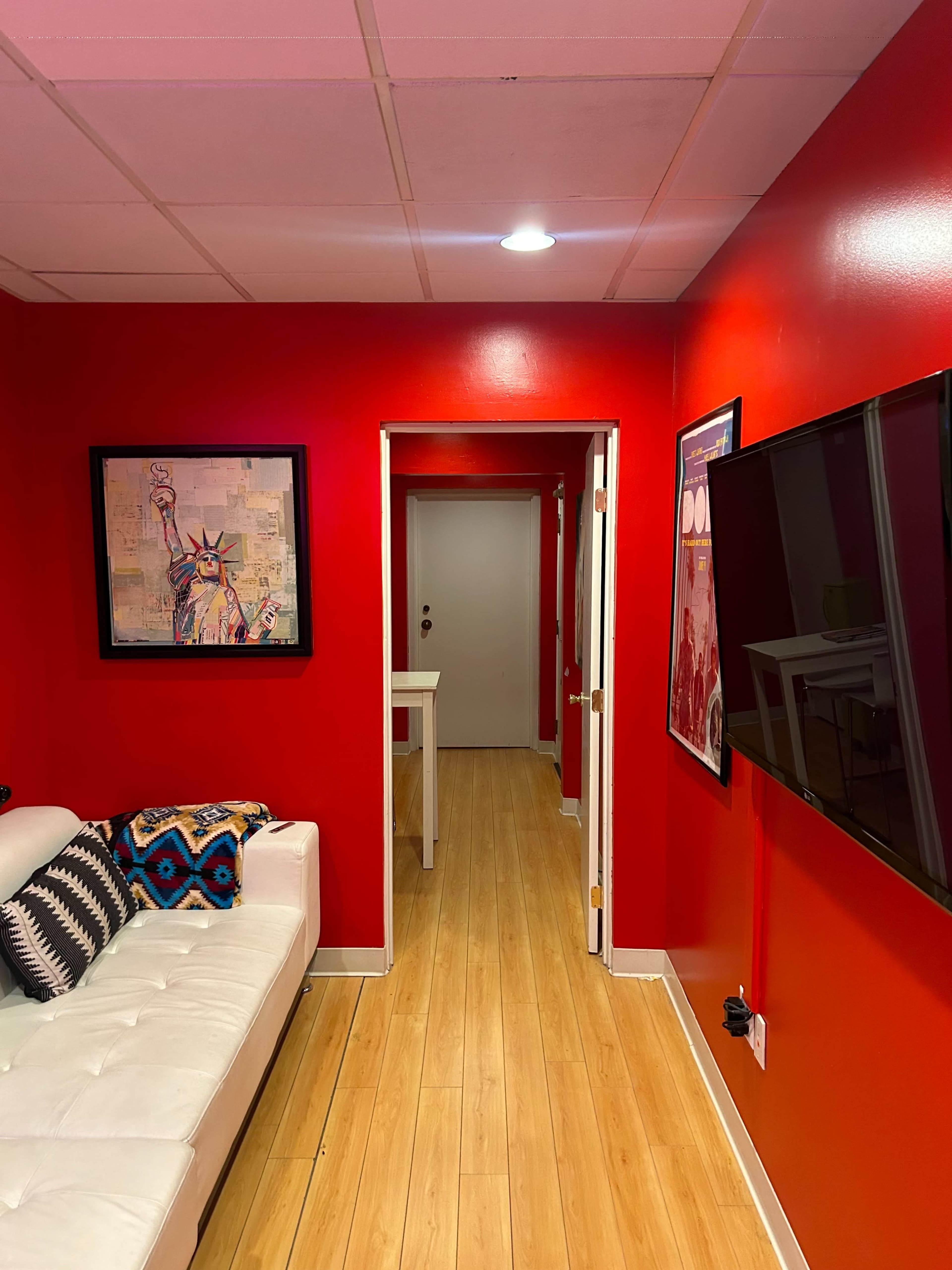 A brightly colored red hallway leads to a door at the end, with a white couch and framed artwork on the wall.