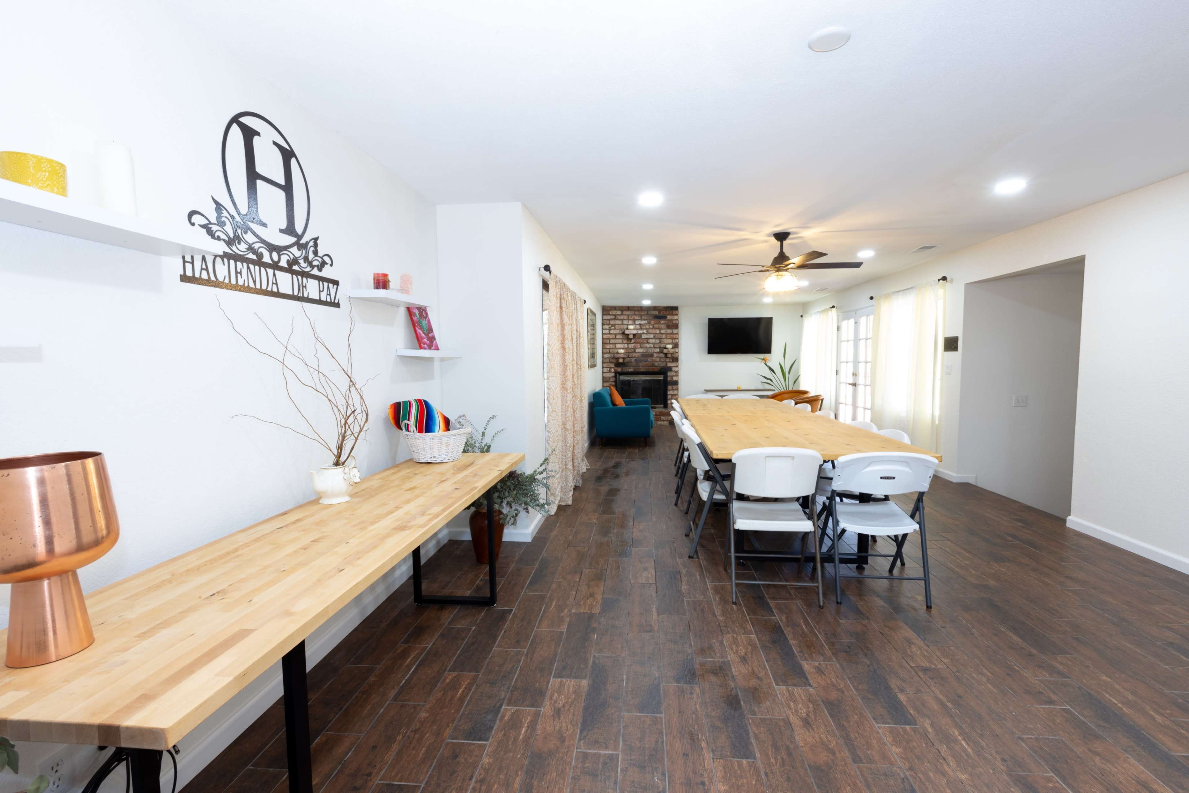 A spacious dining area with a long table set for multiple people, wooden flooring, and a wall shelf adorned with decorative items.