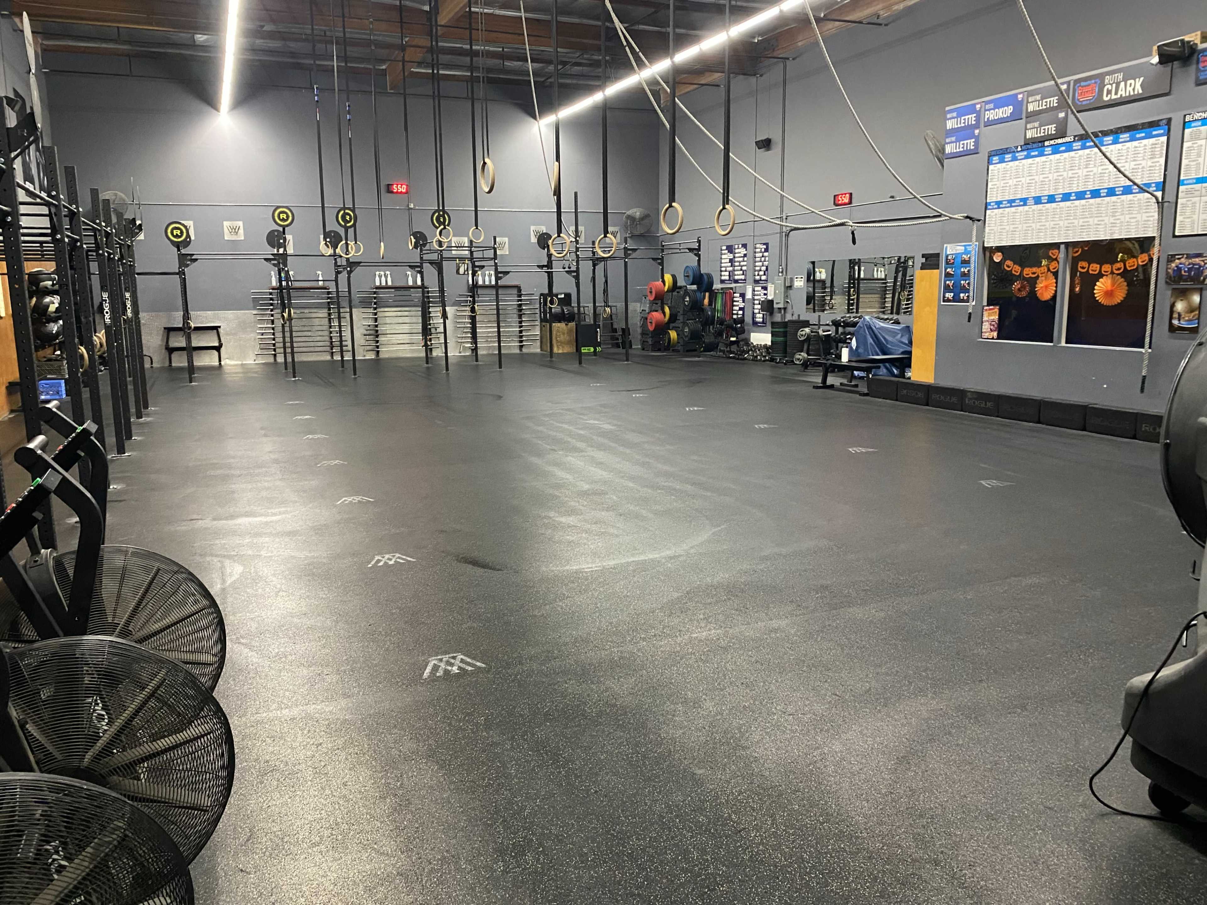 A spacious gym with various workout stations, including pull-up rings and exercise equipment, arranged in a well-lit area with rubber flooring.