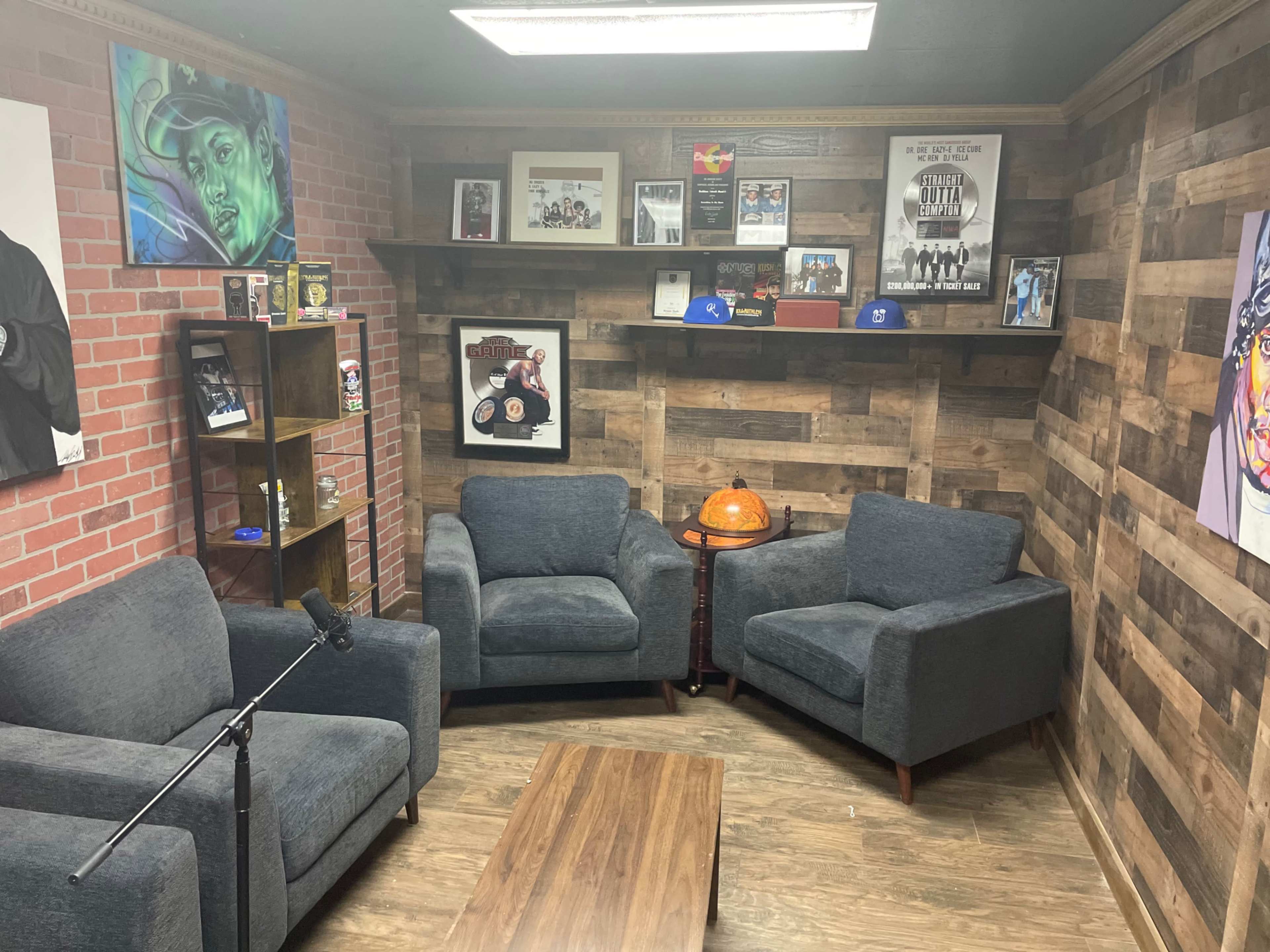 A cozy room with brick and wooden walls, featuring two gray armchairs, a wooden coffee table, a bookshelf displaying framed photos, and various decorations on the walls.