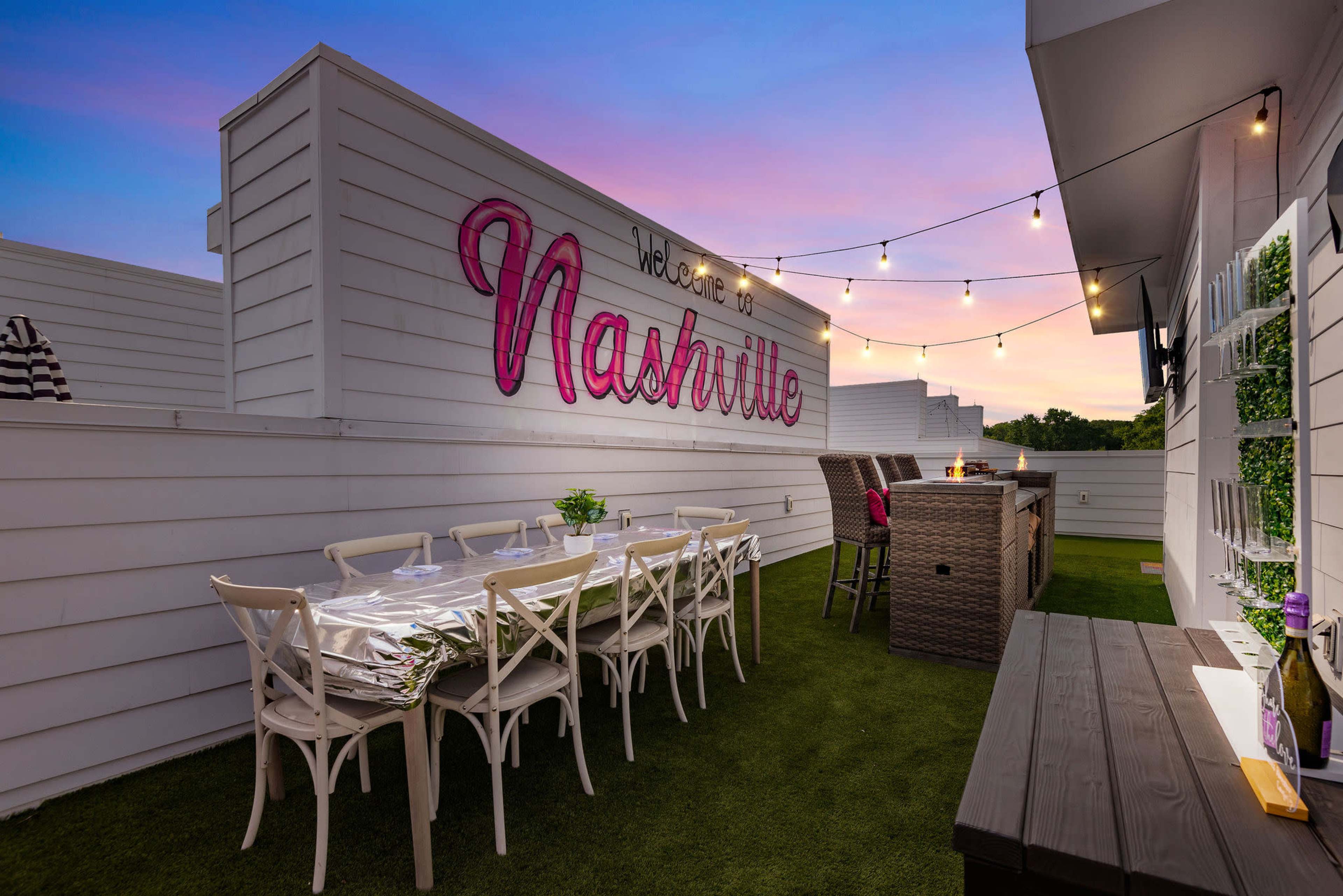 The image shows a rooftop patio in Nashville adorned with string lights, a dining area with white chairs, and a bar setup against a backdrop of a colorful sunset.