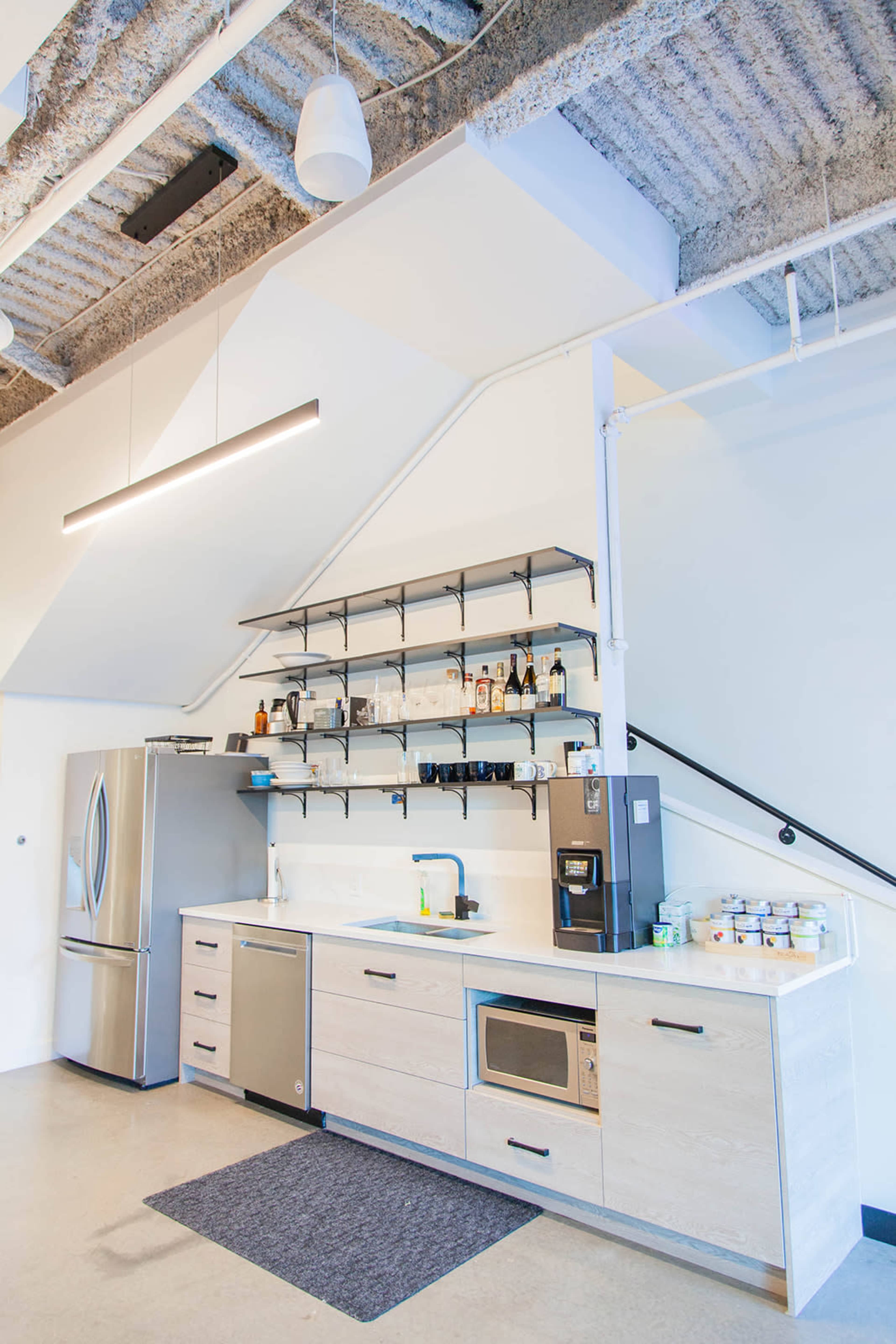 A modern kitchen with stainless steel appliances, a white countertop, and open shelving against a textured ceiling.