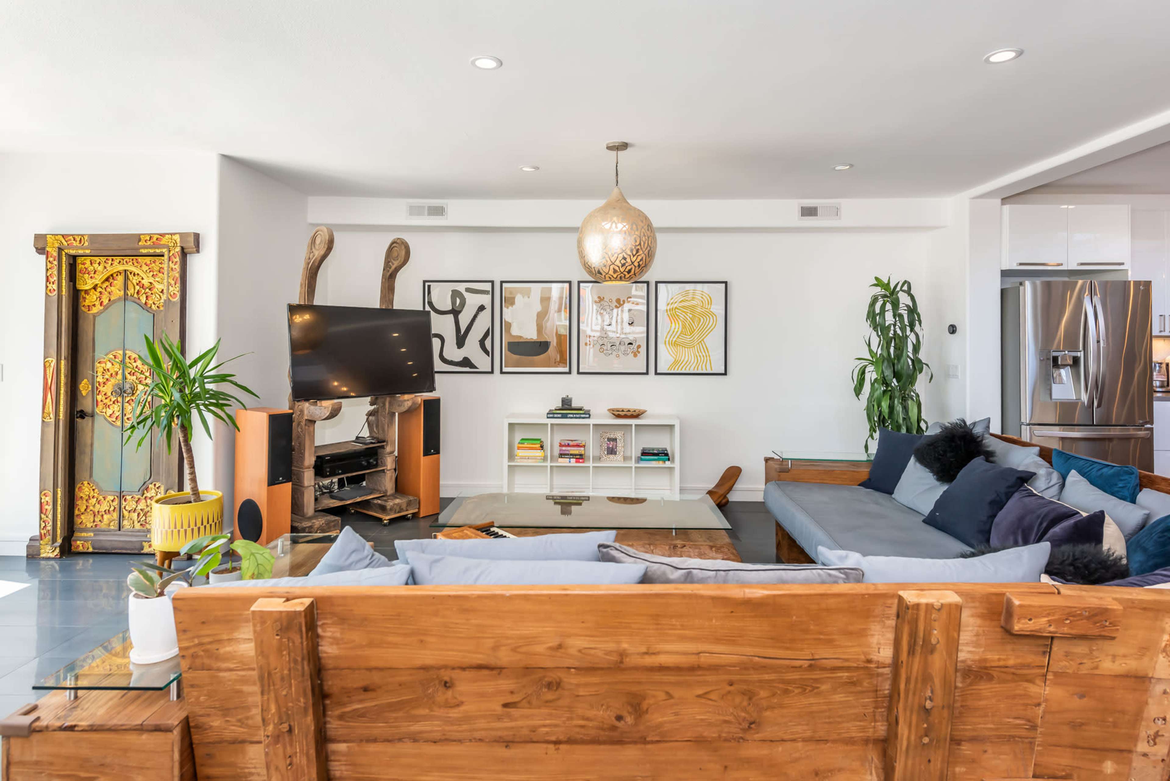 A modern living room featuring a large sectional sofa, a glass coffee table, a television mounted on the wall, and various decorative artworks and plants.
