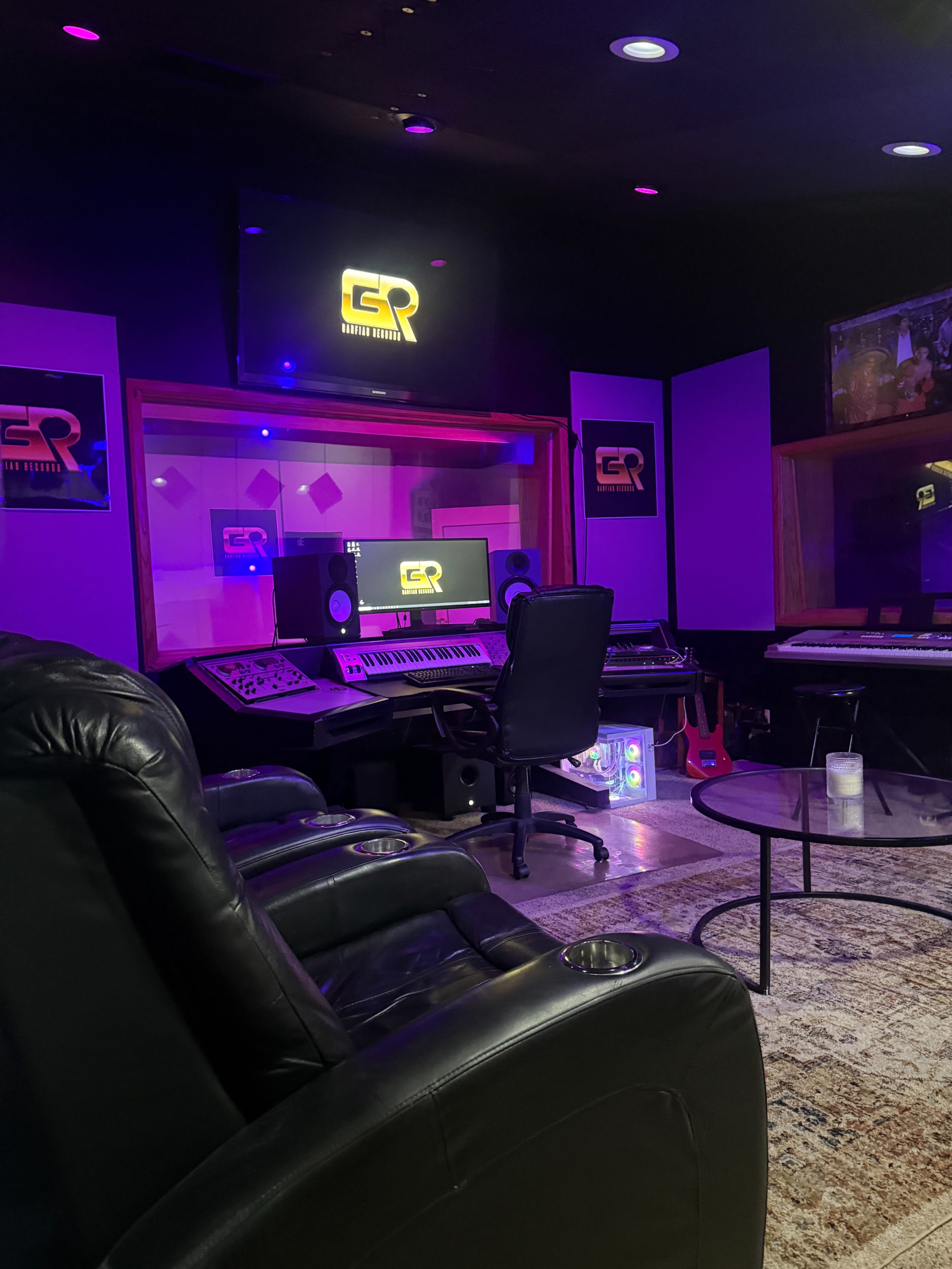 The image shows a music studio with a central control desk, seating area, and colorful lighting.