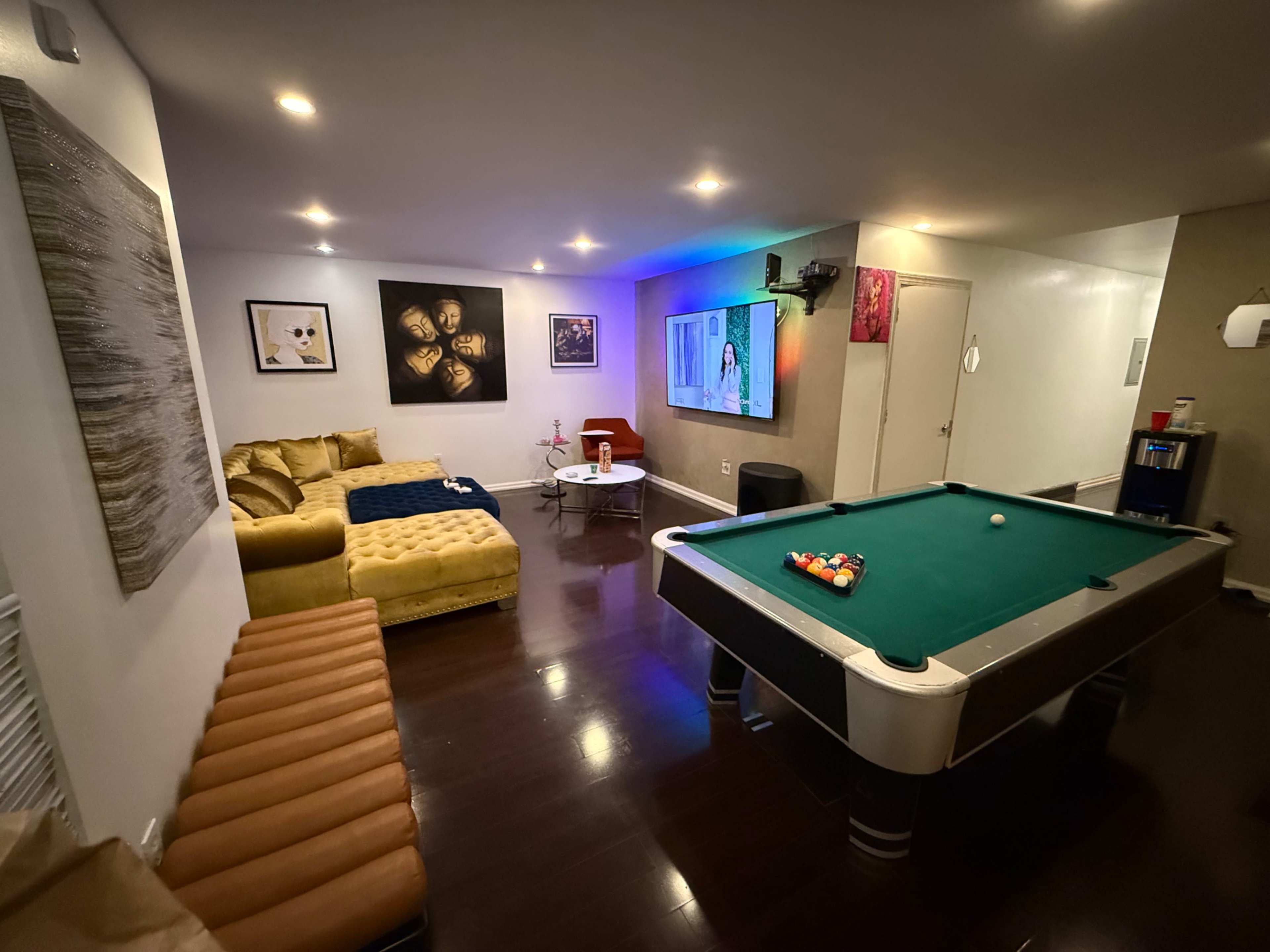 The room features a pool table, a yellow chaise lounge, and a small table arranged with artwork on the walls.