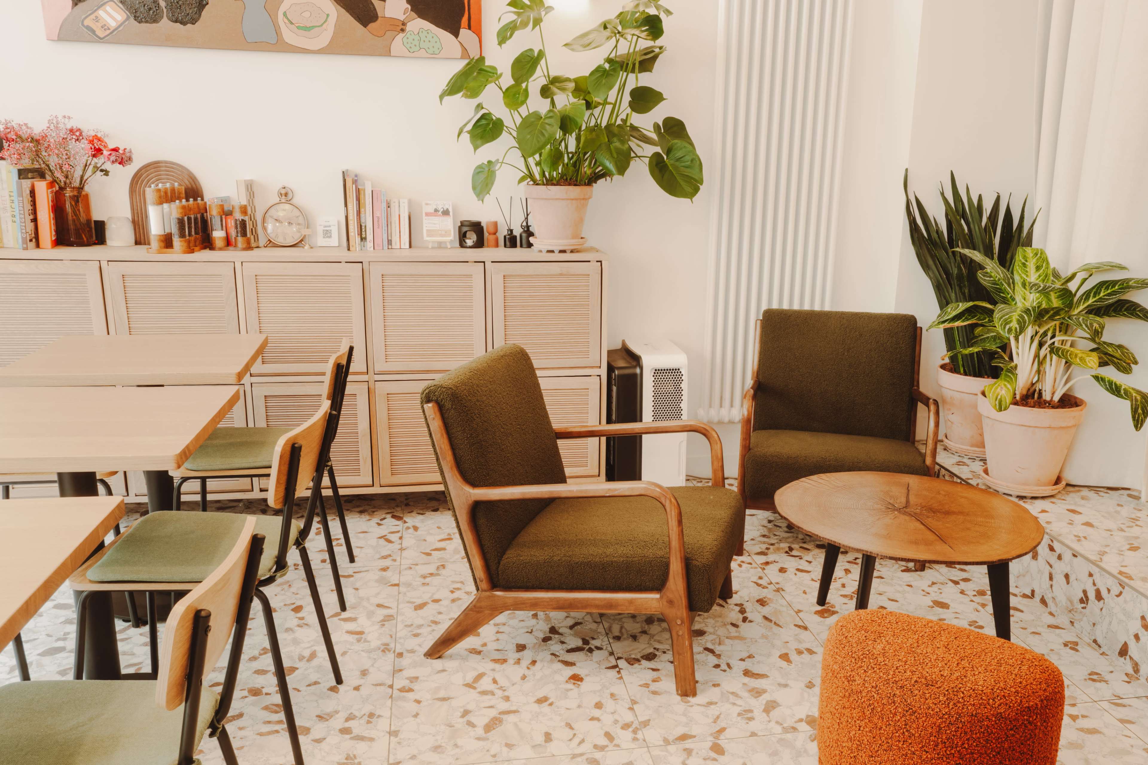 The image depicts a cozy café interior featuring wooden chairs, a circular table, a plant, and a neatly organized shelf in the background.