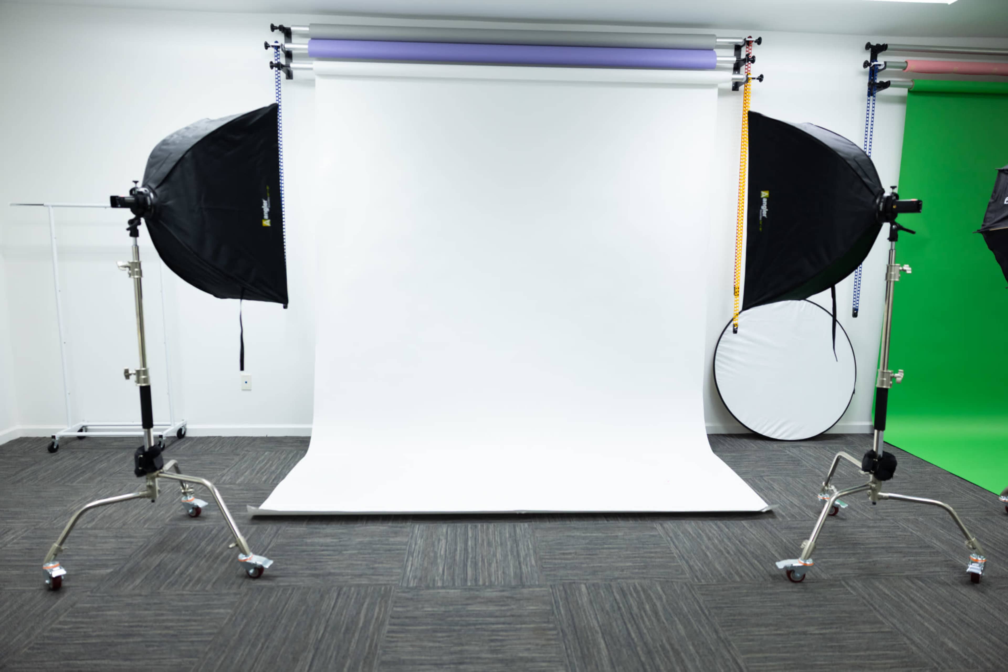 The image shows a photography studio with a white backdrop, two large softbox lights on tripods, and a circular reflector on the floor.
