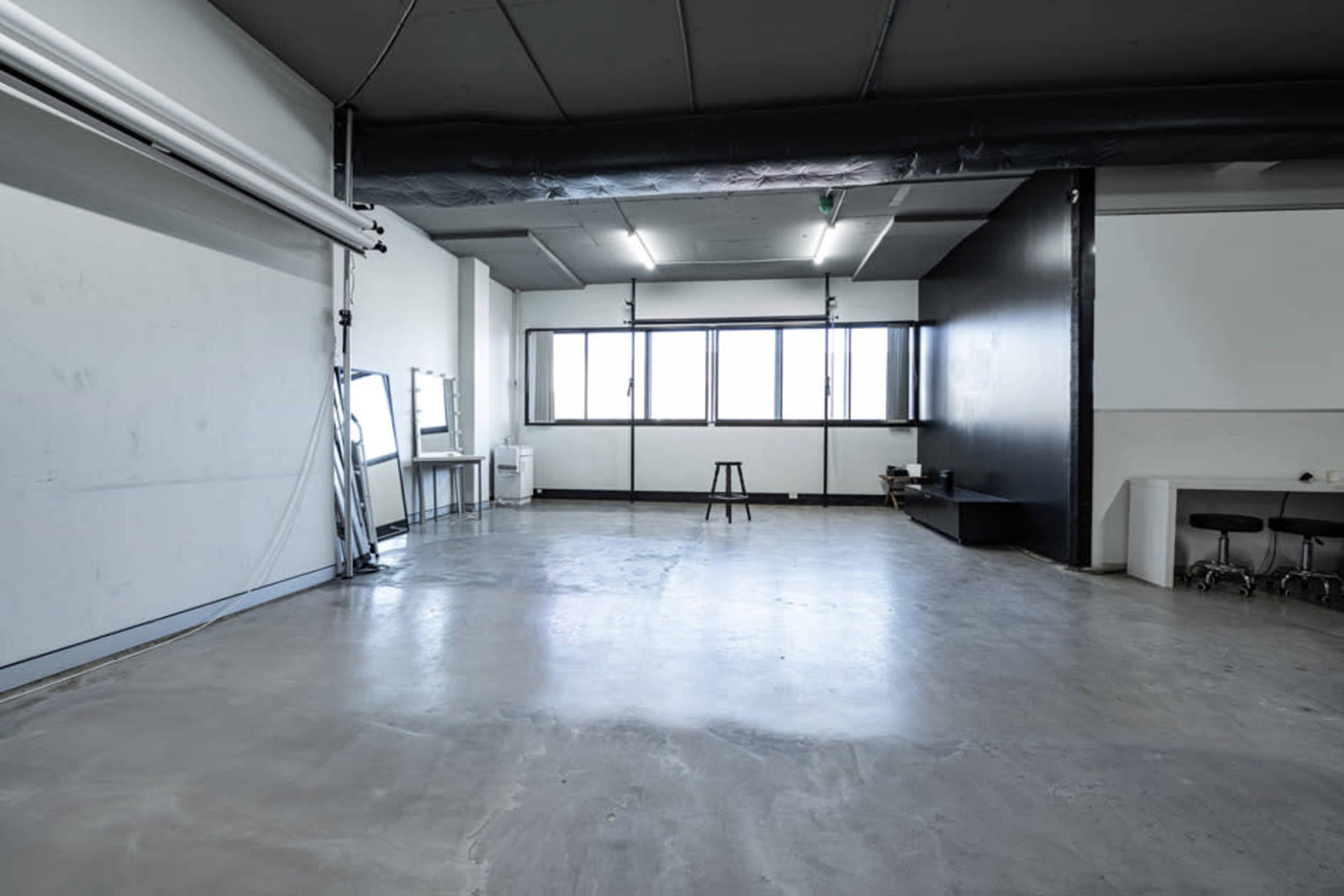 A spacious, empty room with concrete flooring, large windows, and minimal furnishings.