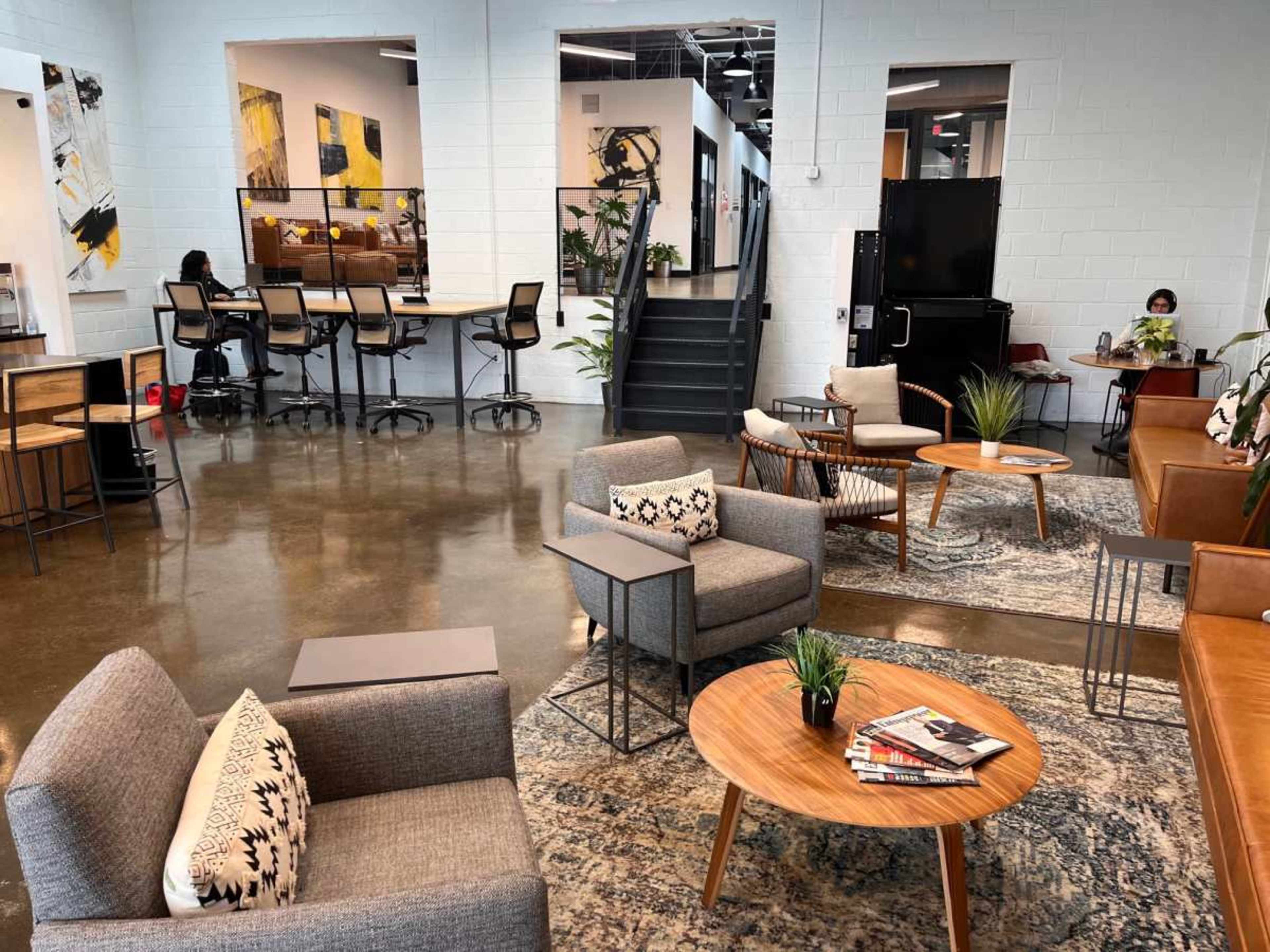A modern coworking space with seating areas, wooden furniture, and stairs leading to another level.