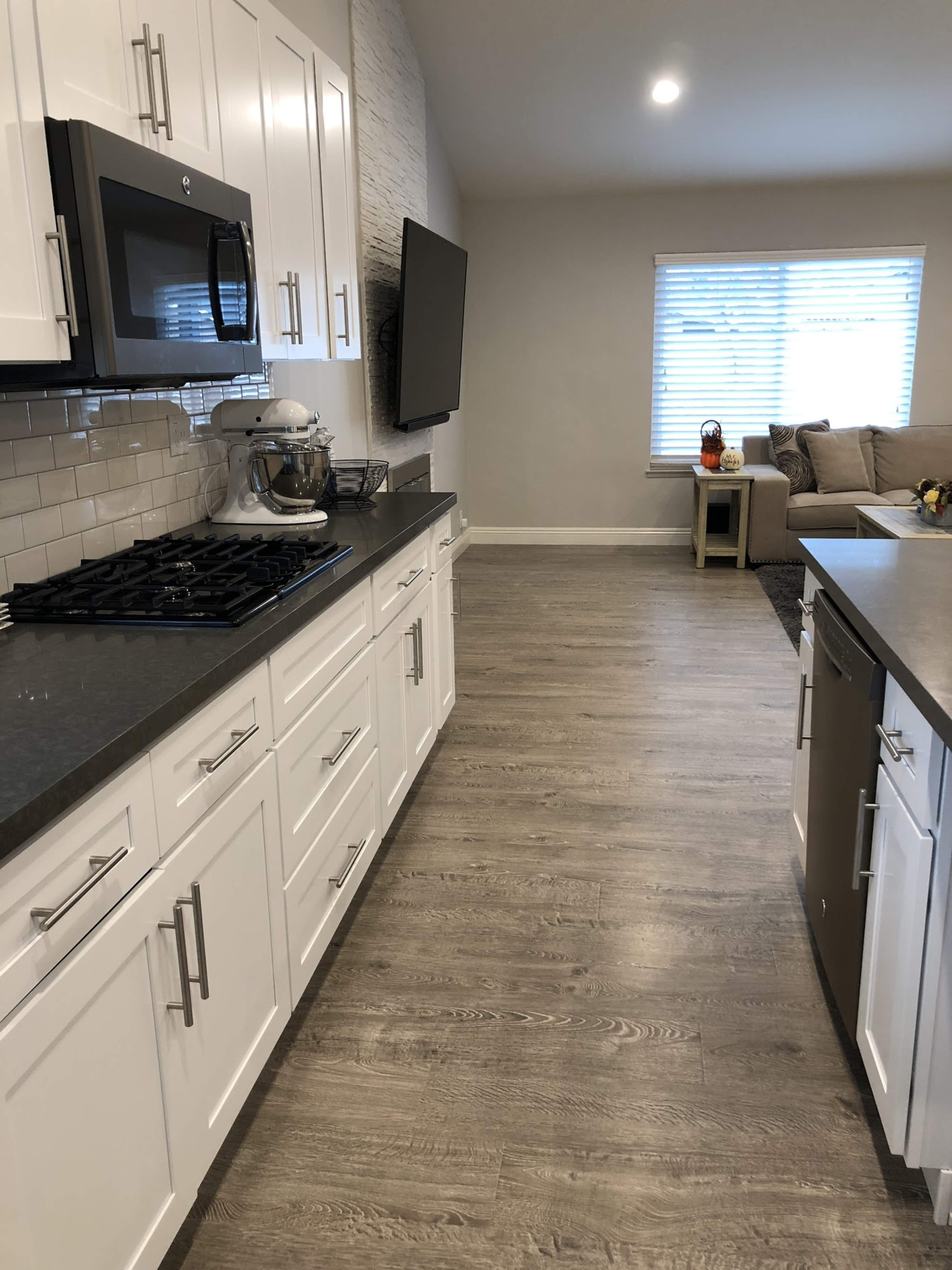 A modern kitchen with white cabinetry, a gas stove, and a living area visible in the background with a couch and a window.