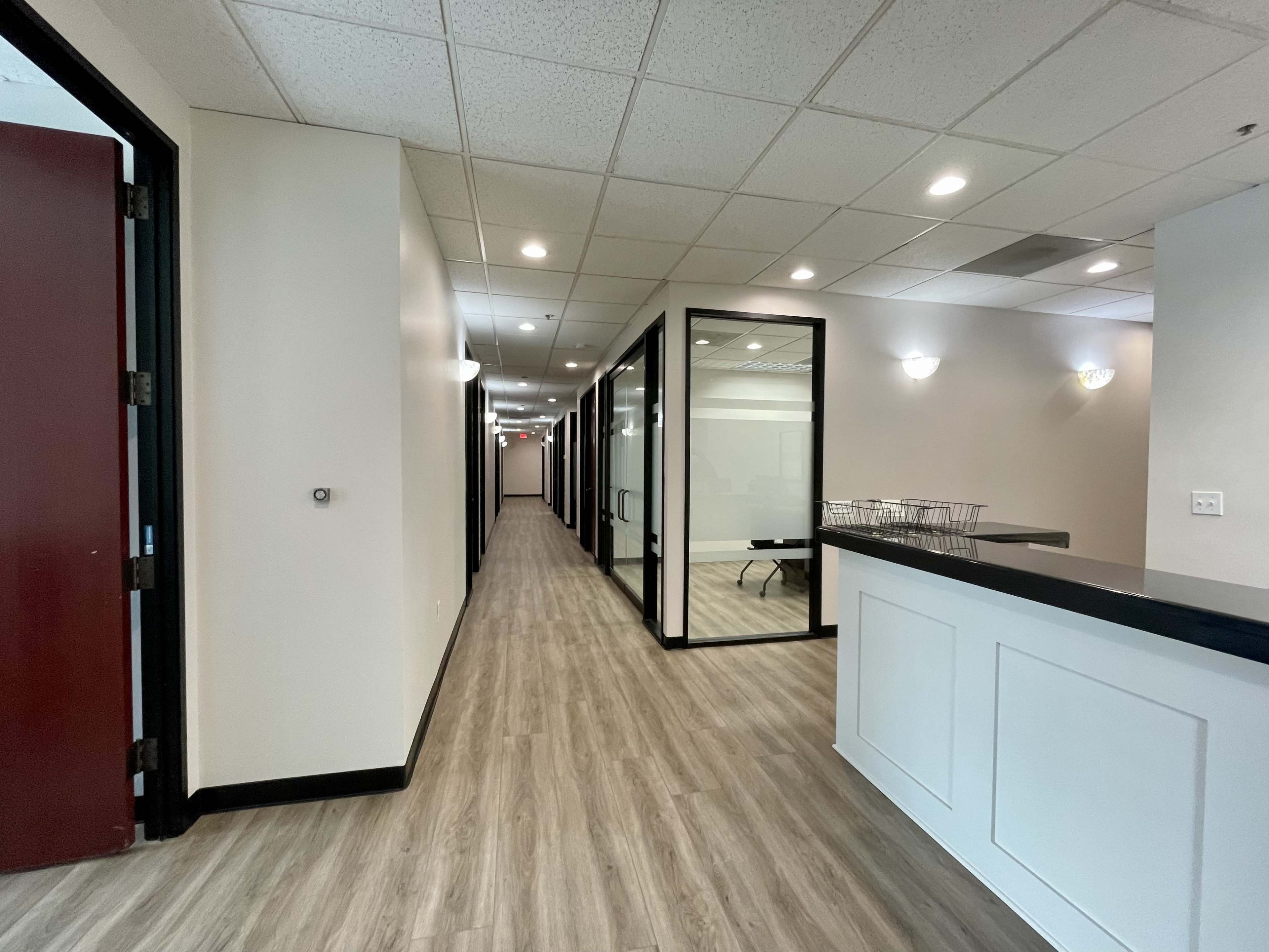 A long hallway with glass-walled offices on one side and a reception area with a counter at the end.