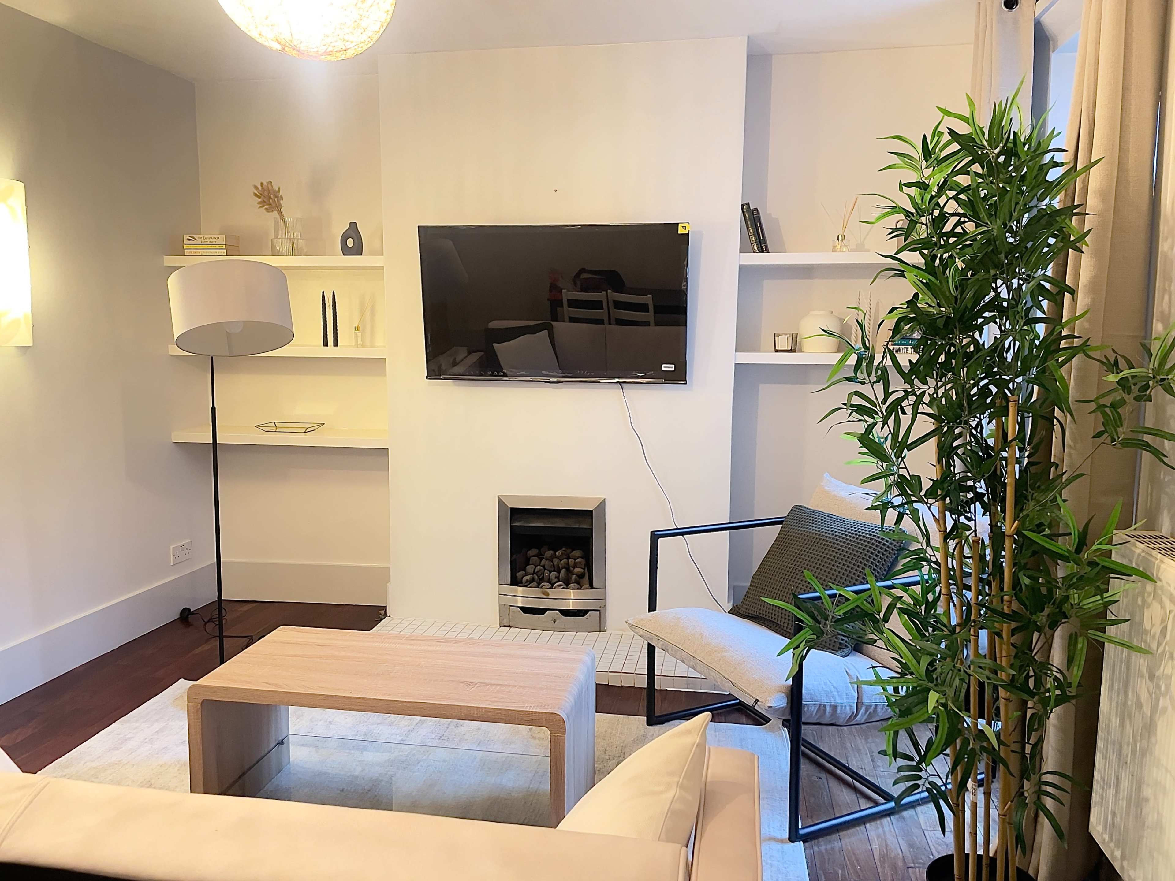 A modern living room with a television mounted on the wall, a light-colored sofa, a coffee table, and plants arranged around a simple decor.