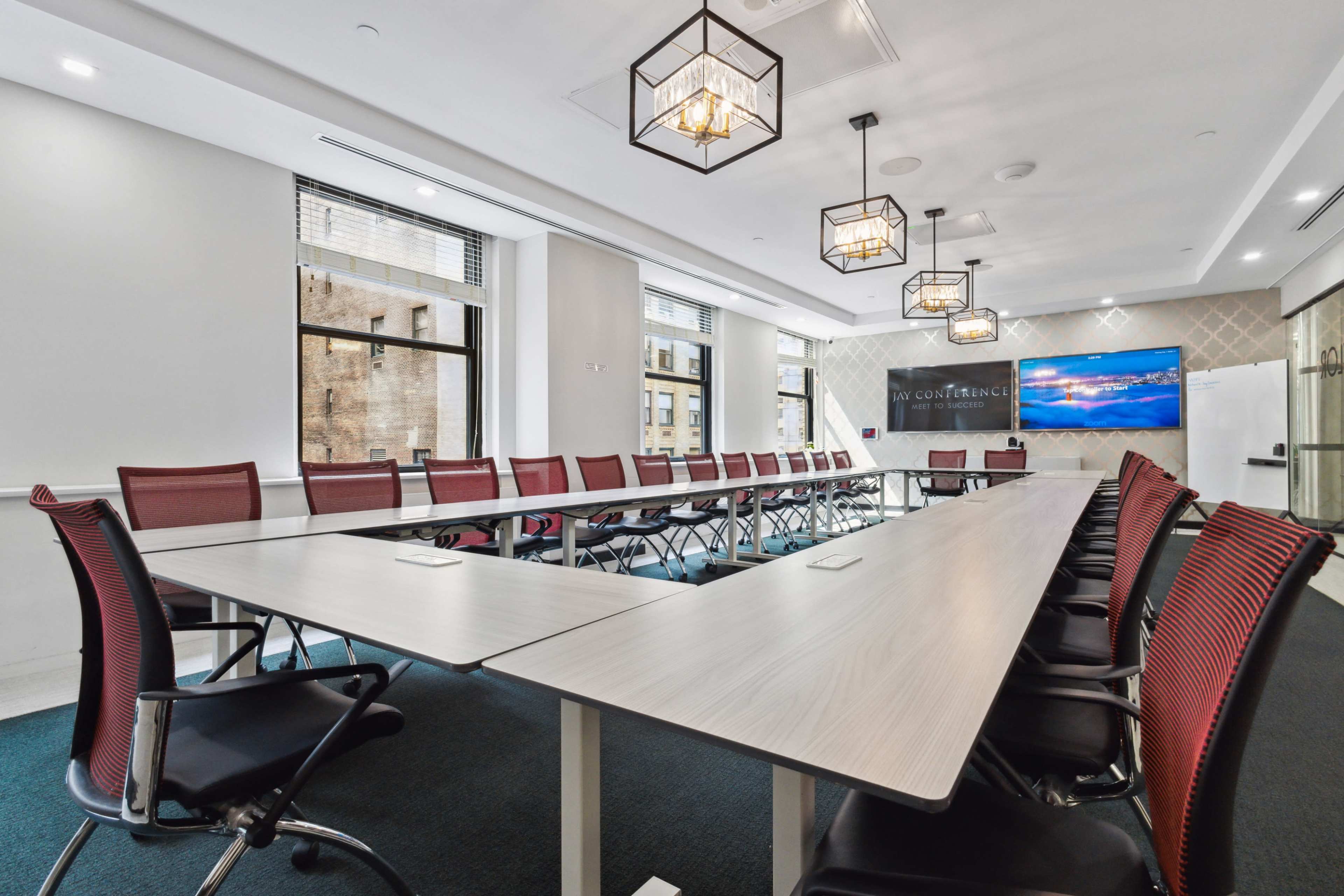 A long, U-shaped conference table is set up in a well-lit meeting room with modern chairs and a large screen at one end.