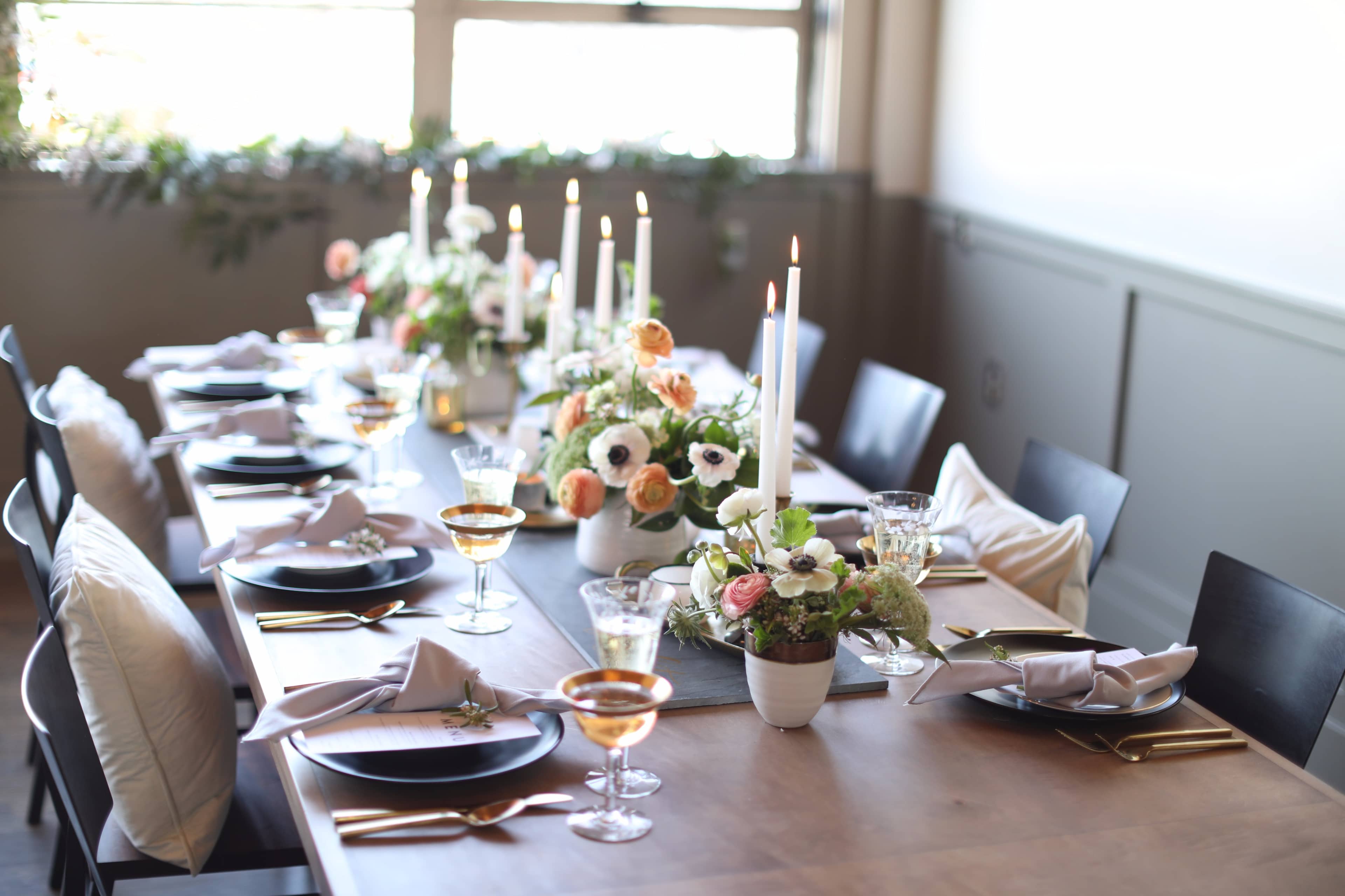 A beautifully arranged dining table featuring elegant floral centerpieces, white candles in holders, and polished tableware set for a gathering.