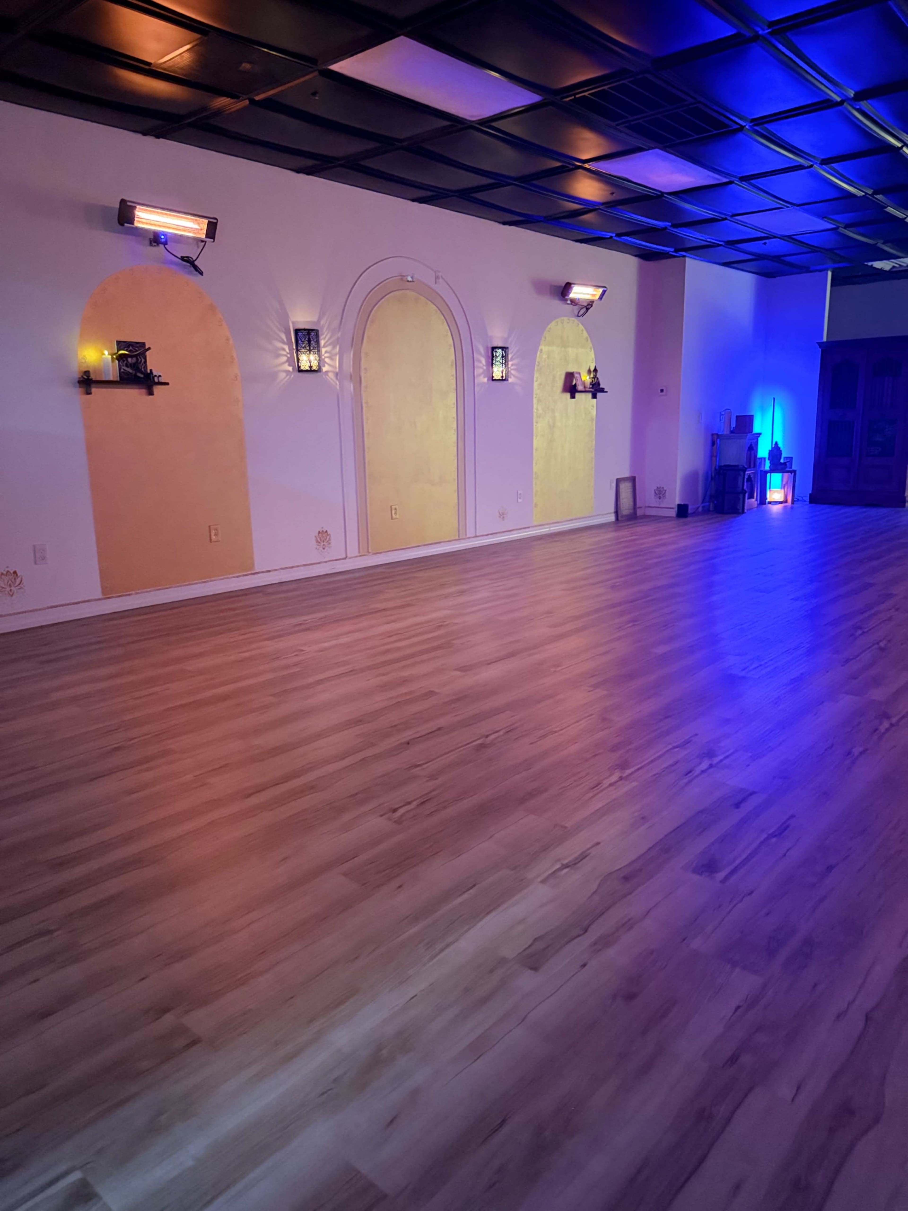 The image shows a bright, spacious room with wooden flooring, featuring three archways on the wall and ambient lighting in hues of blue and purple.
