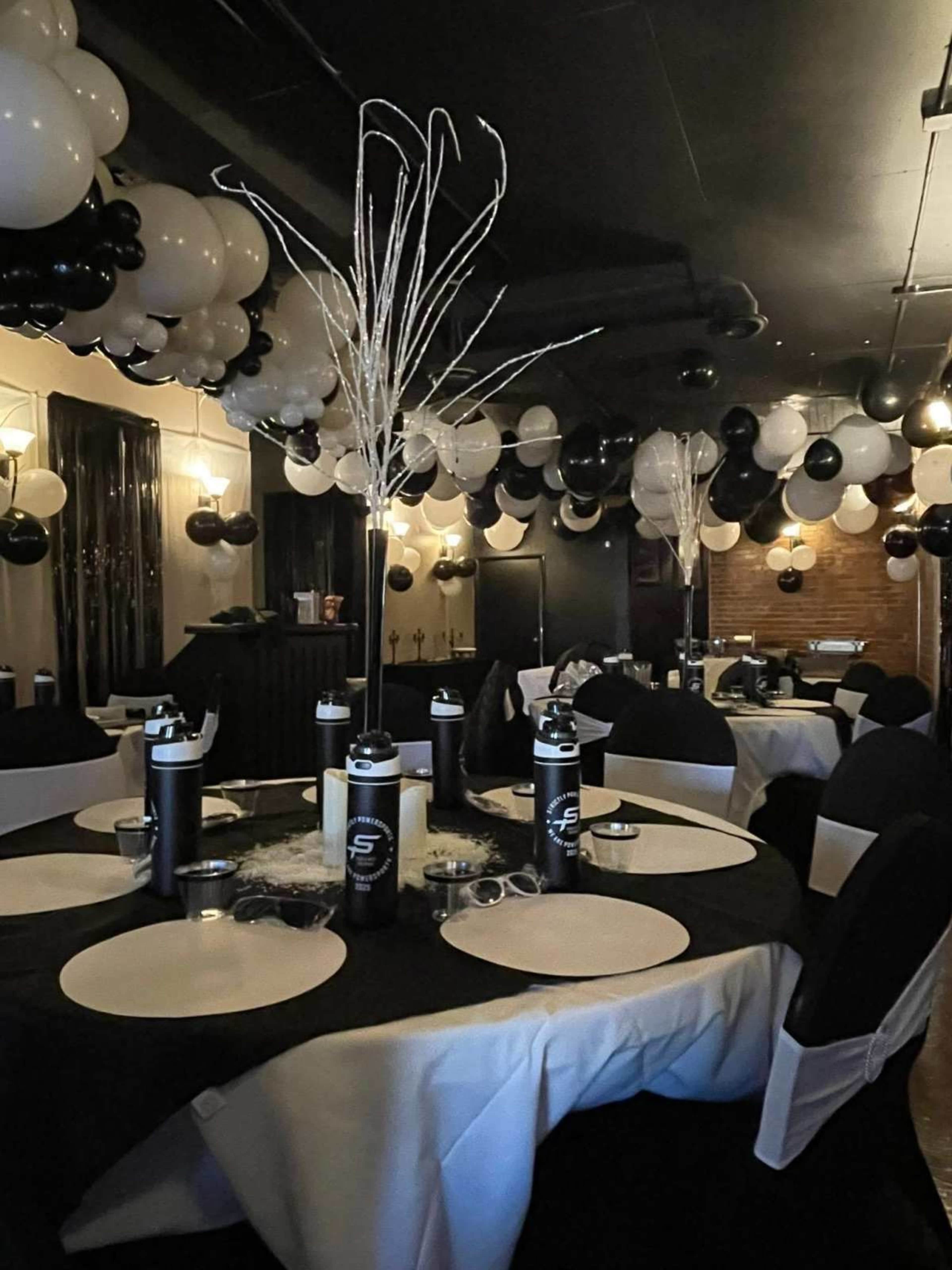 The scene features a banquet hall decorated with black and white balloons, elegantly arranged tables, and centerpiece decorations.
