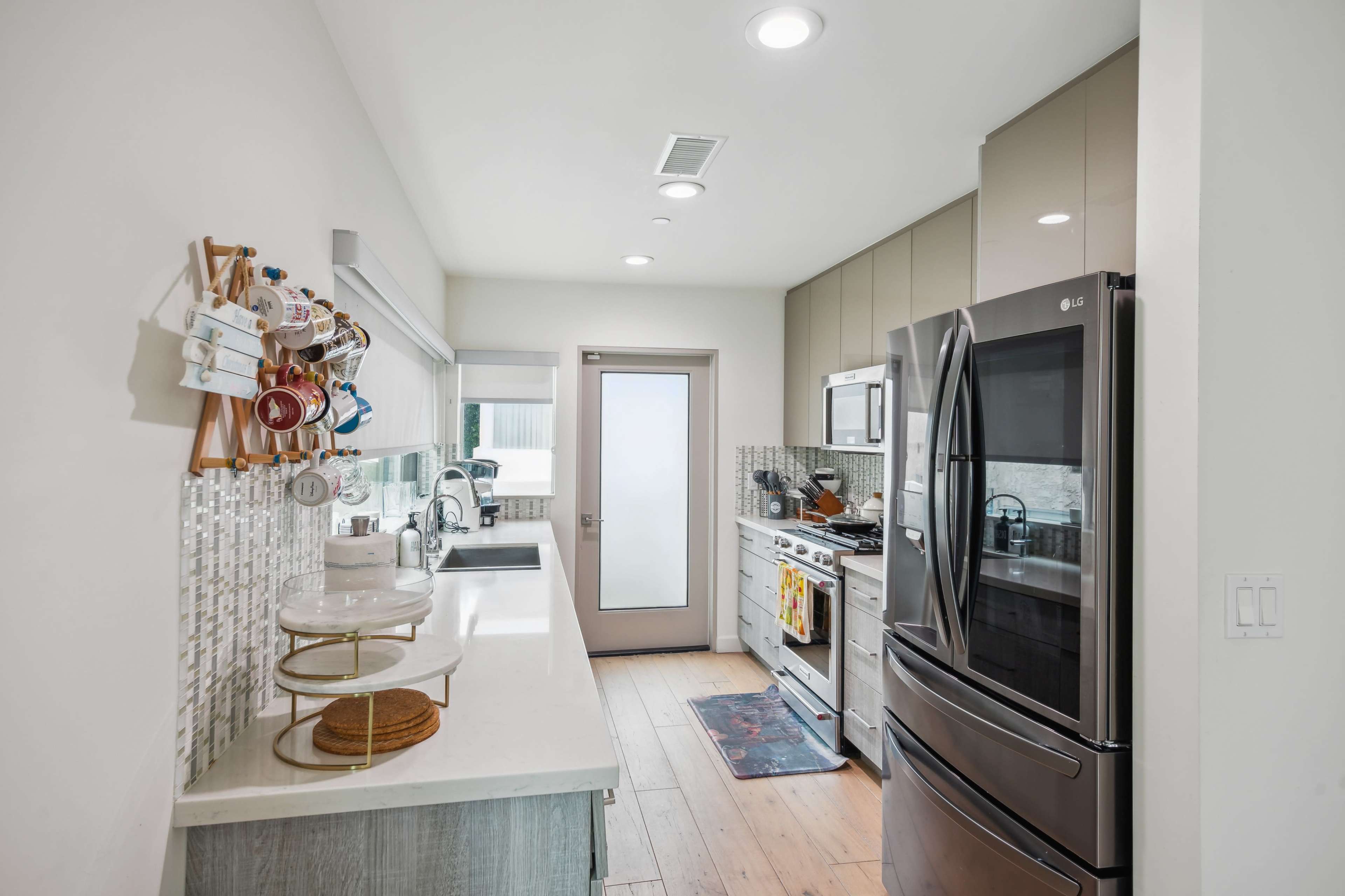 A modern kitchen with stainless steel appliances, a white countertop, and a tile backsplash, featuring a door leading outside.