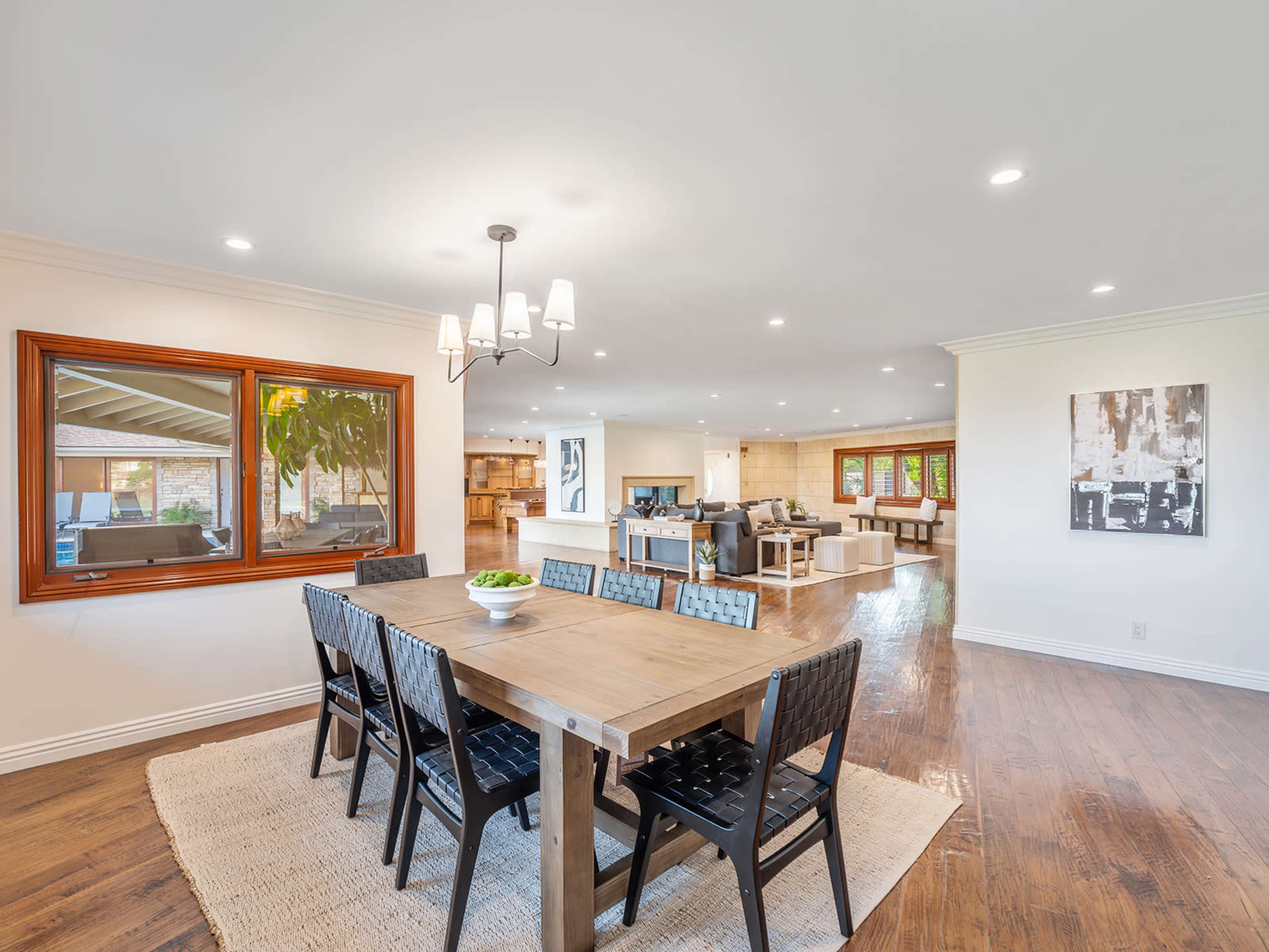 A dining area features a large wooden table surrounded by black chairs, with an open layout connecting to a living space and kitchen in the background.