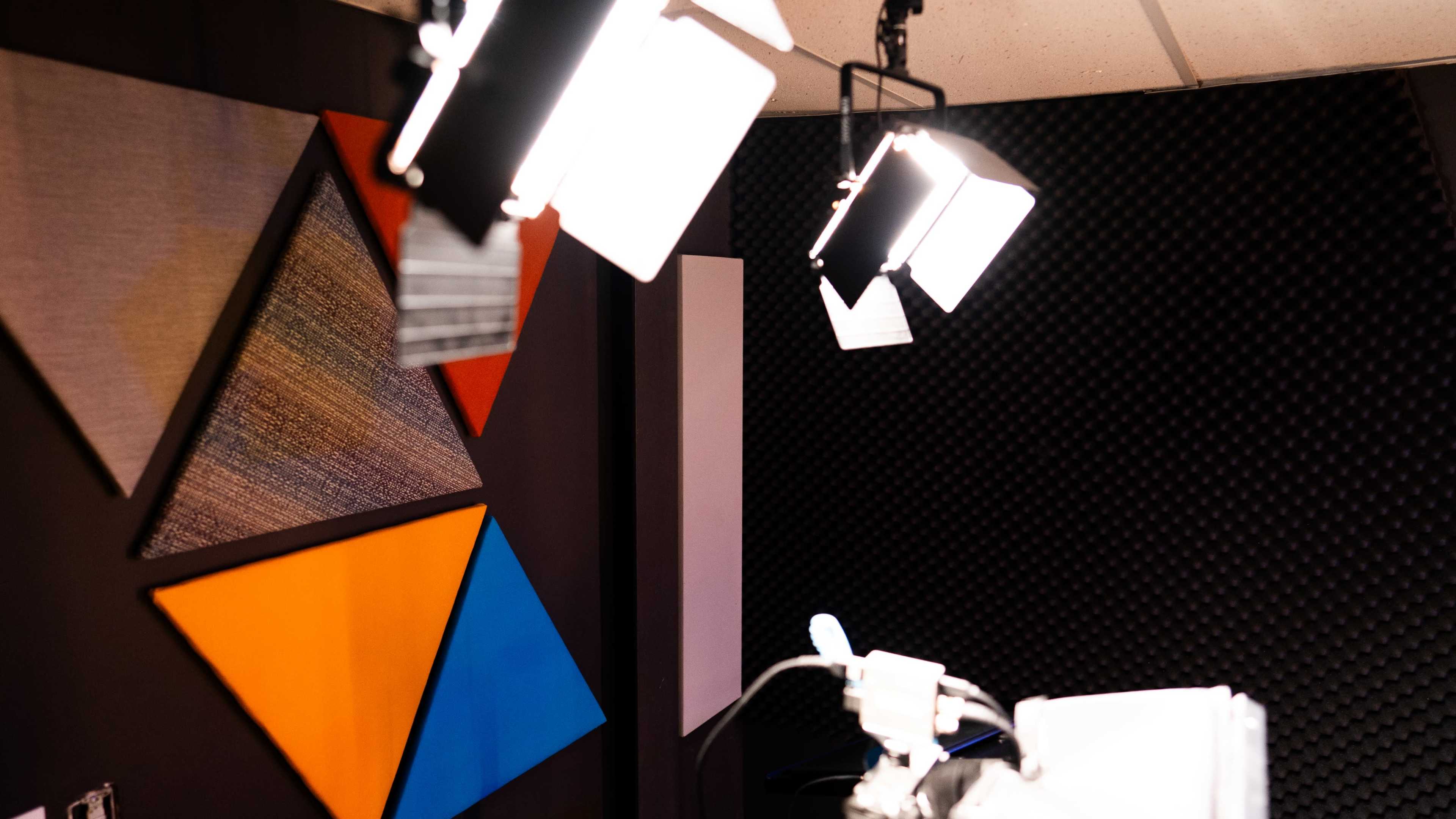 A studio setting with geometric fabric panels on the wall and several bright lights overhead.