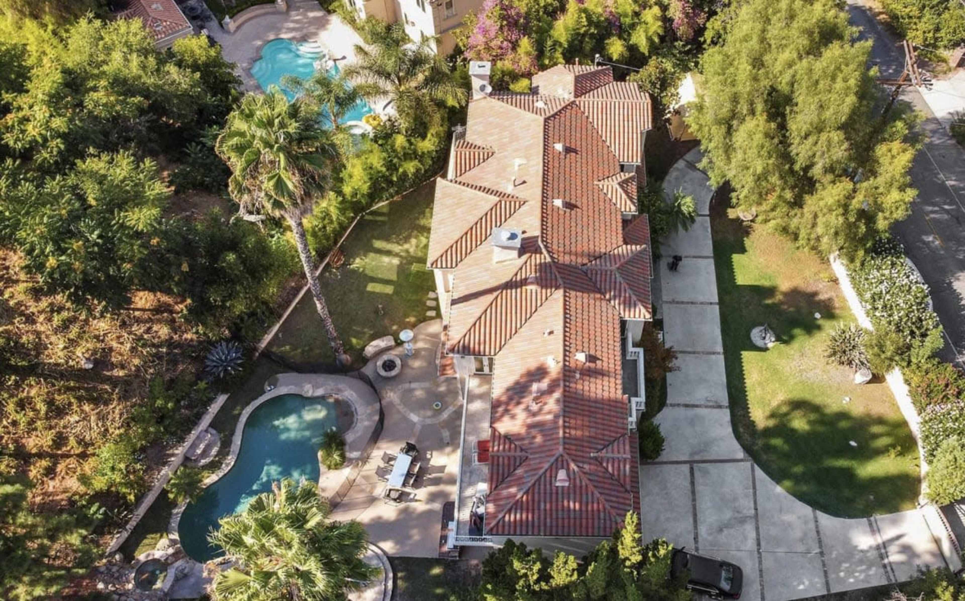 The image shows an aerial view of a large residential property featuring a swimming pool, landscaped garden, and a driveway.