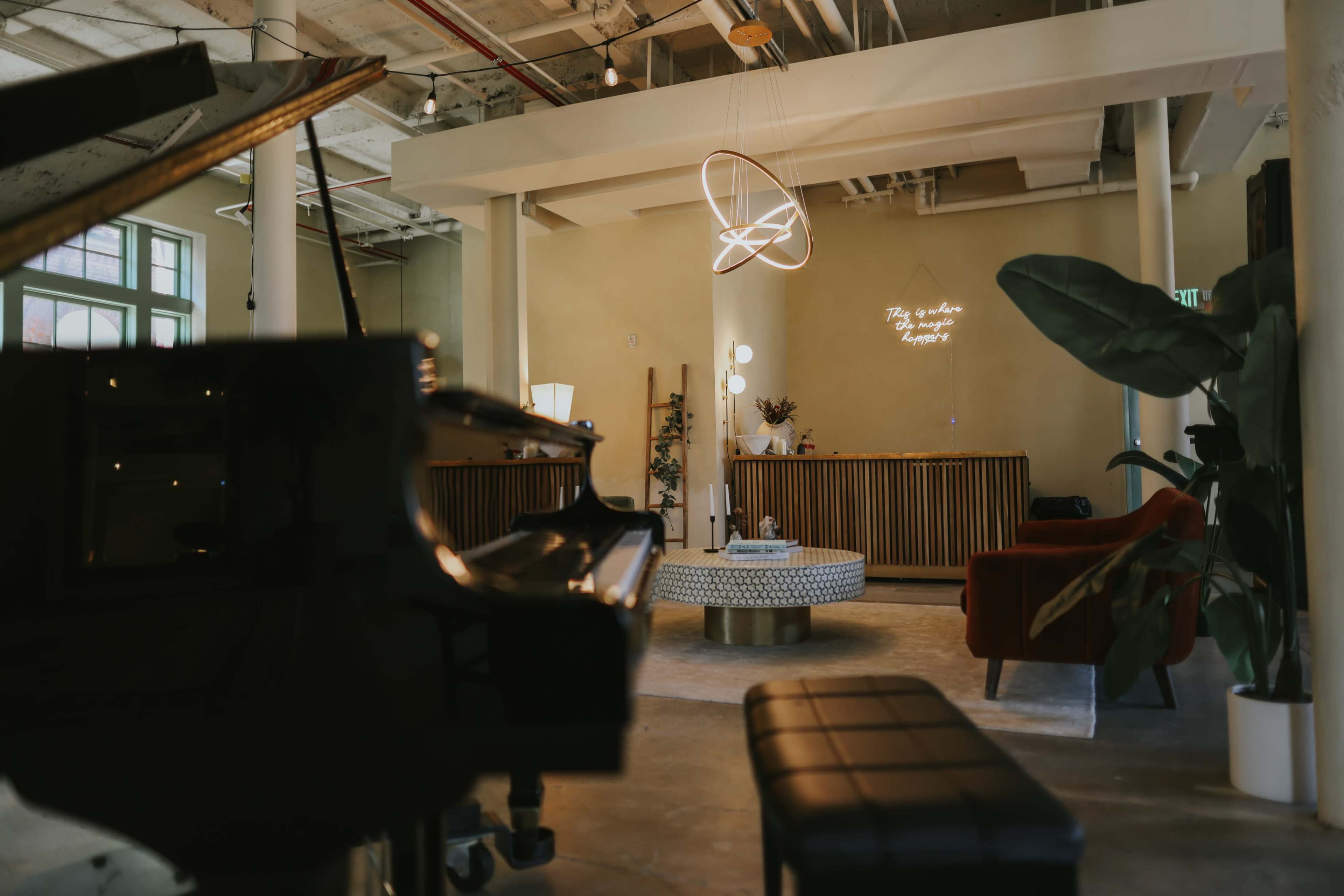 A spacious indoor lounge features a grand piano, a circular coffee table, and modern decor with a pendant light hanging above.