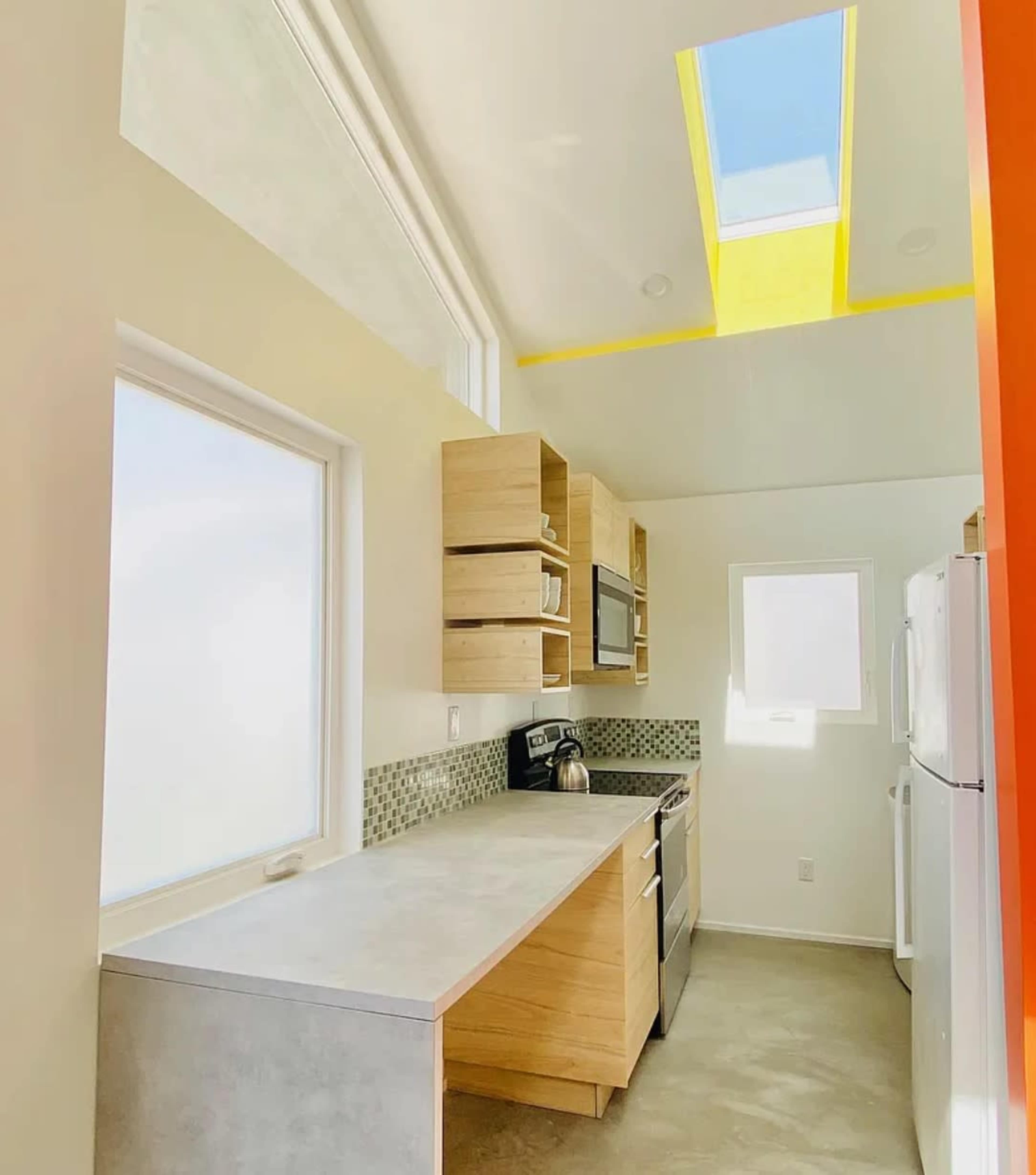 A modern kitchen features wooden cabinets, stainless steel appliances, and large windows that provide natural light.