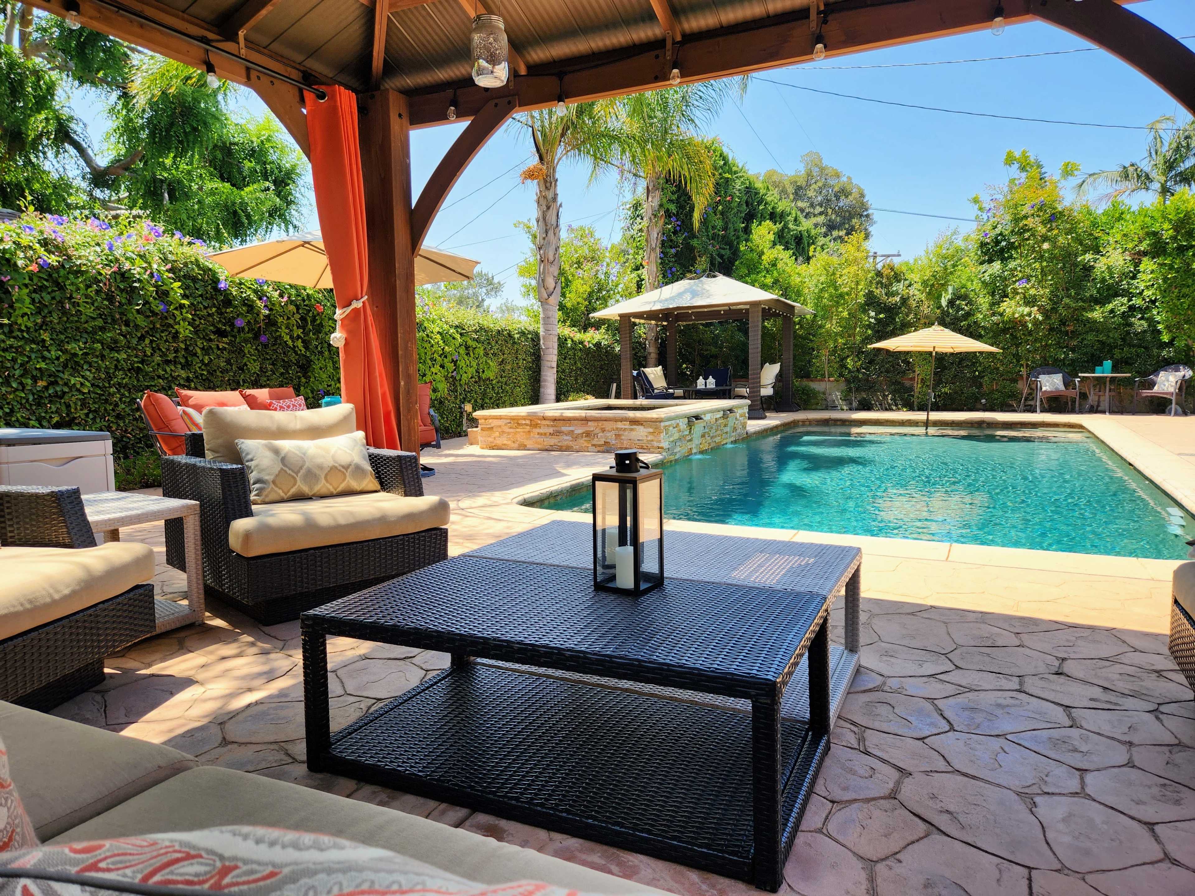 A patio area with wicker furniture, a coffee table, and a swimming pool surrounded by palm trees and sun loungers.