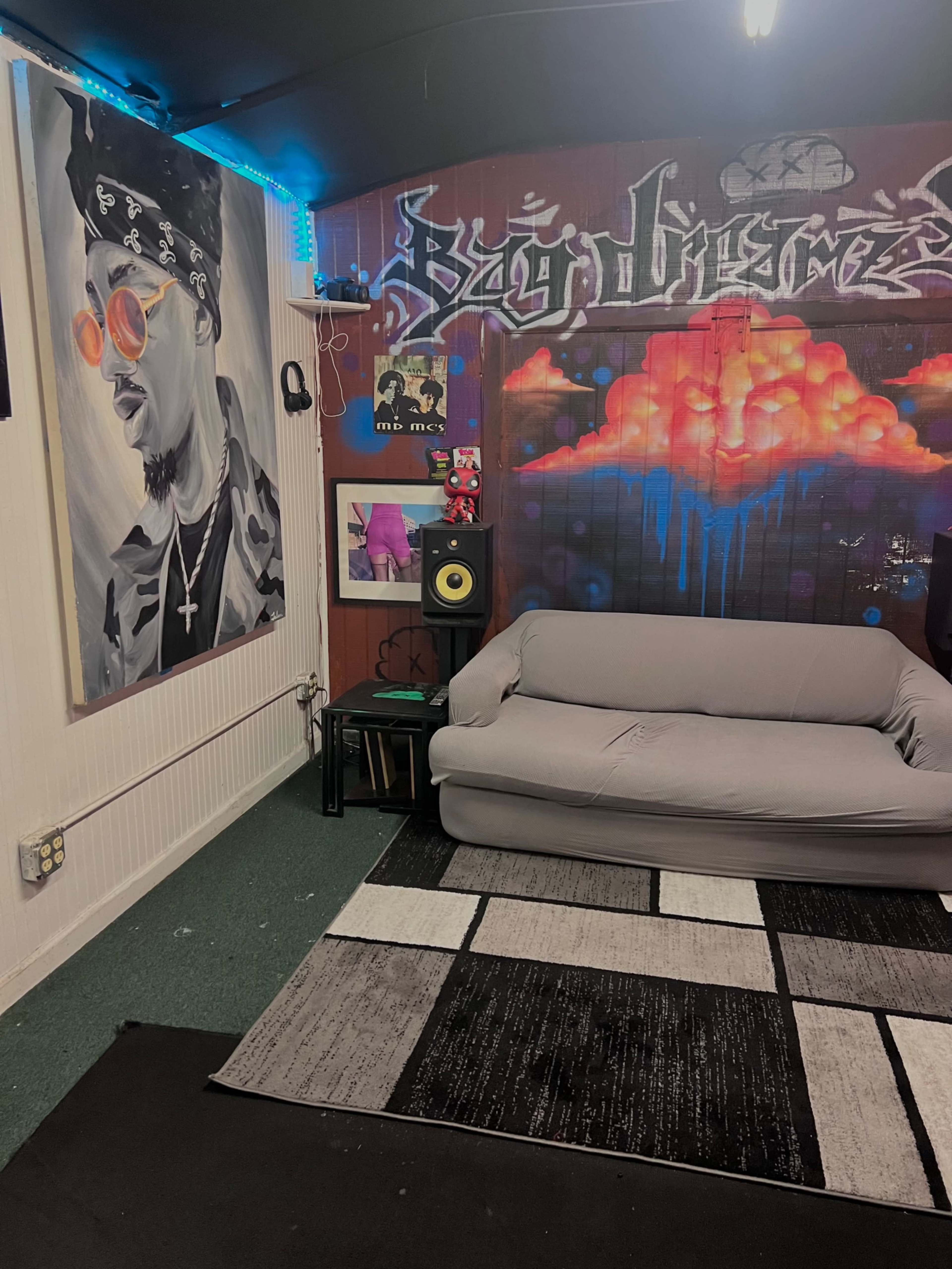 The image shows a small room featuring a couch, a large painted mural on the wall, and a sound system setup.