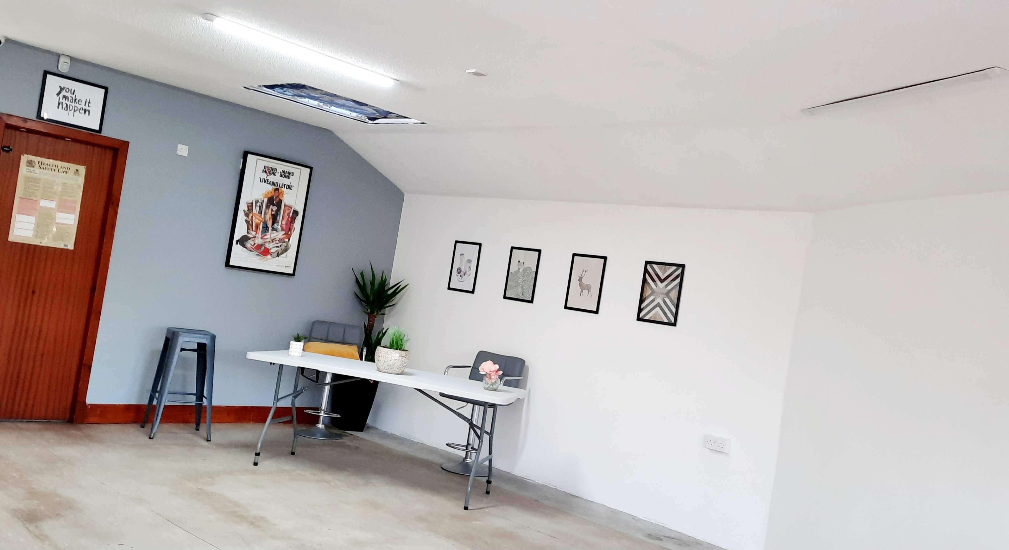 A minimalist room with a table, chairs, framed artworks on the wall, and a potted plant.