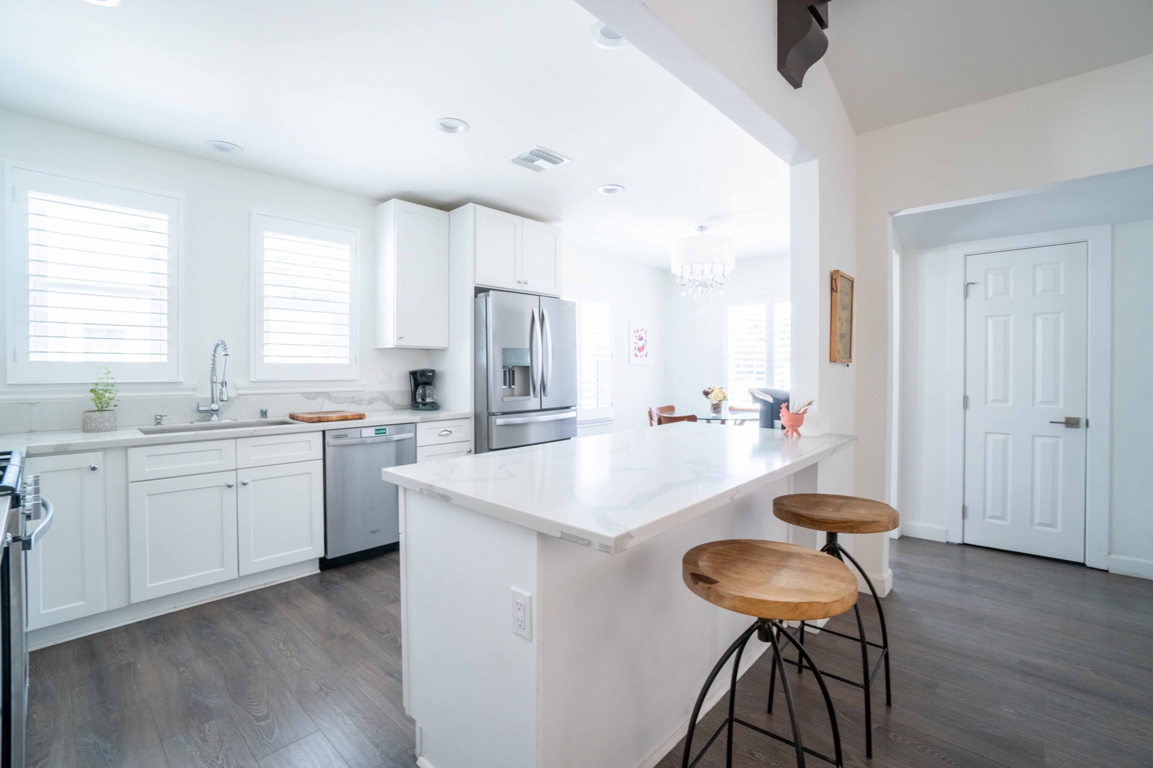 A modern kitchen featuring white cabinets, stainless steel appliances, and a countertop with two bar stools, adjacent to a dining area.
