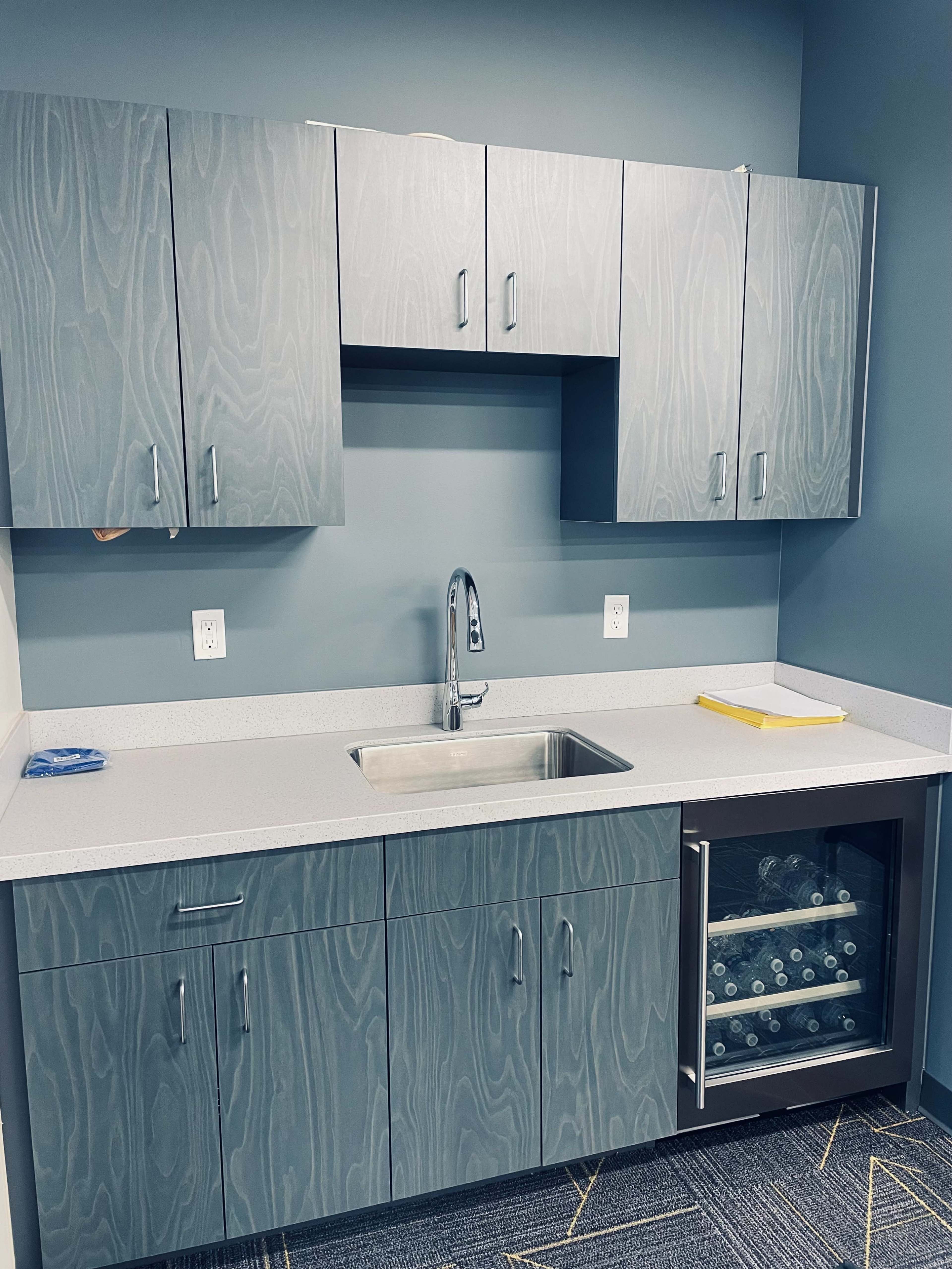 A modern kitchen area with gray cabinetry, a sink, and a small refrigerator below.